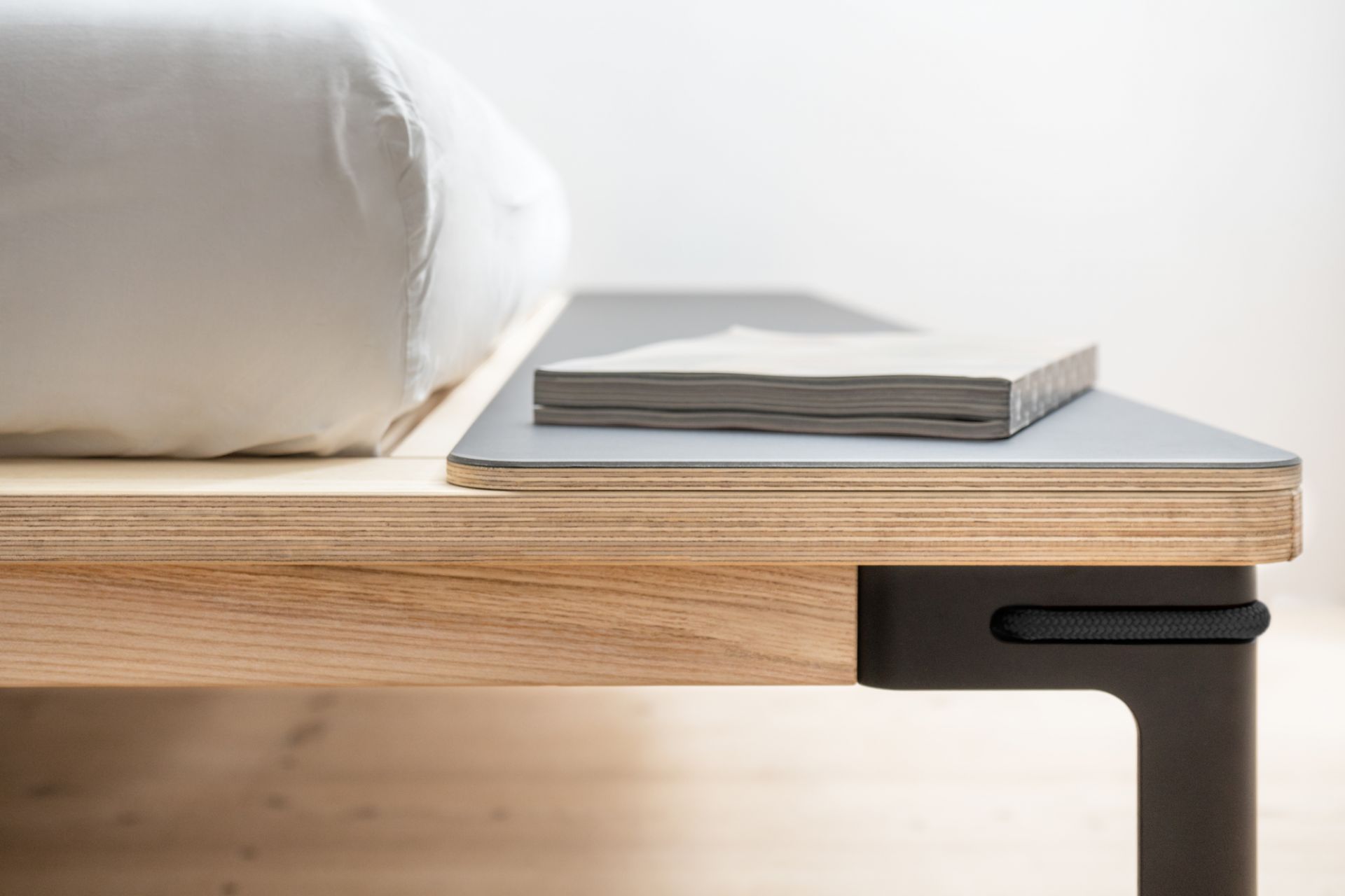 Detailaufnahme vom Moormann Seiltänzer Bett mit Buch und Kissen. Design Bett aus Holz.