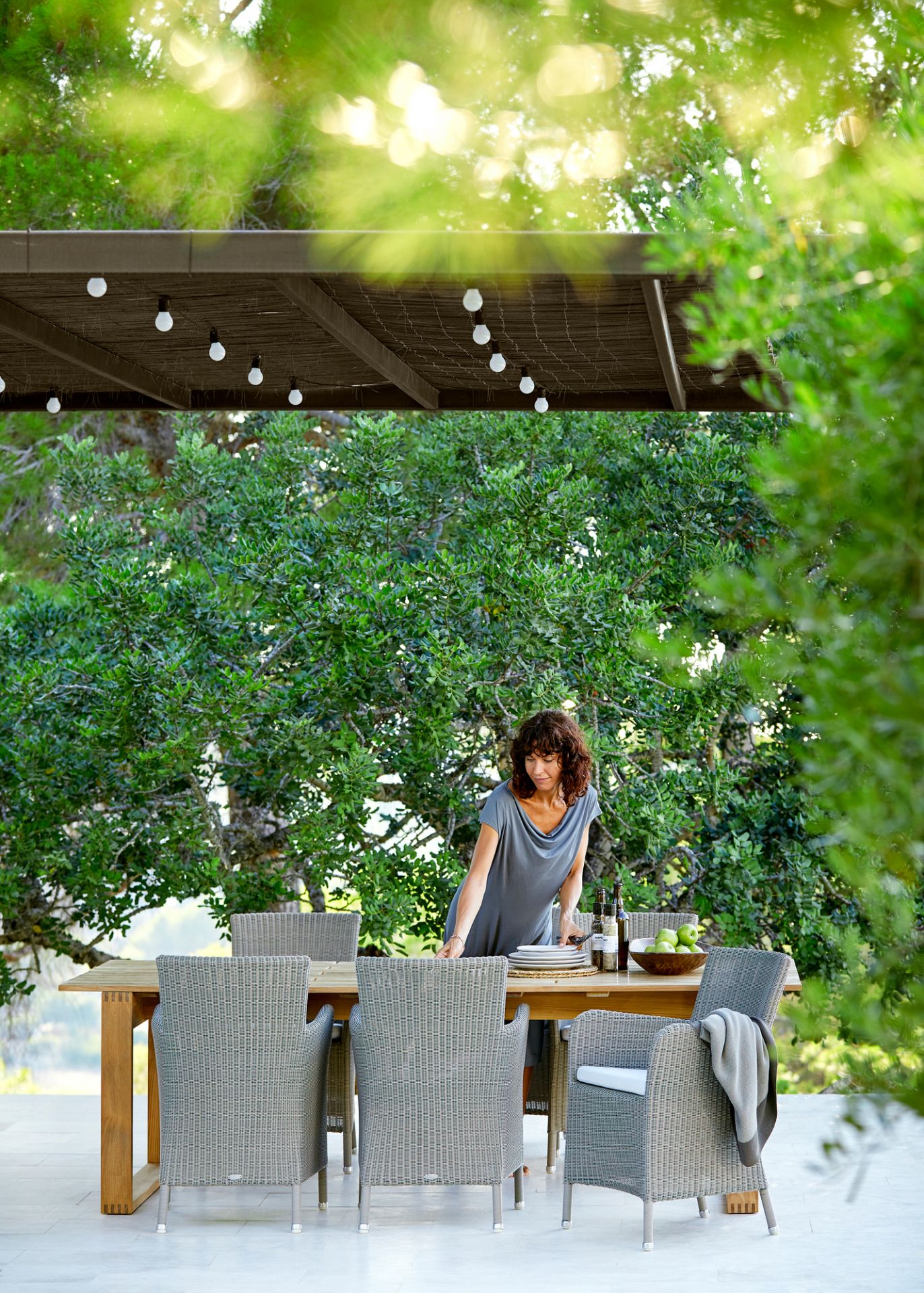 Hampsted Outdoor Sessel von Cane-Line auf Terrasse mit Esstisch und Frau beim Tischdecken.