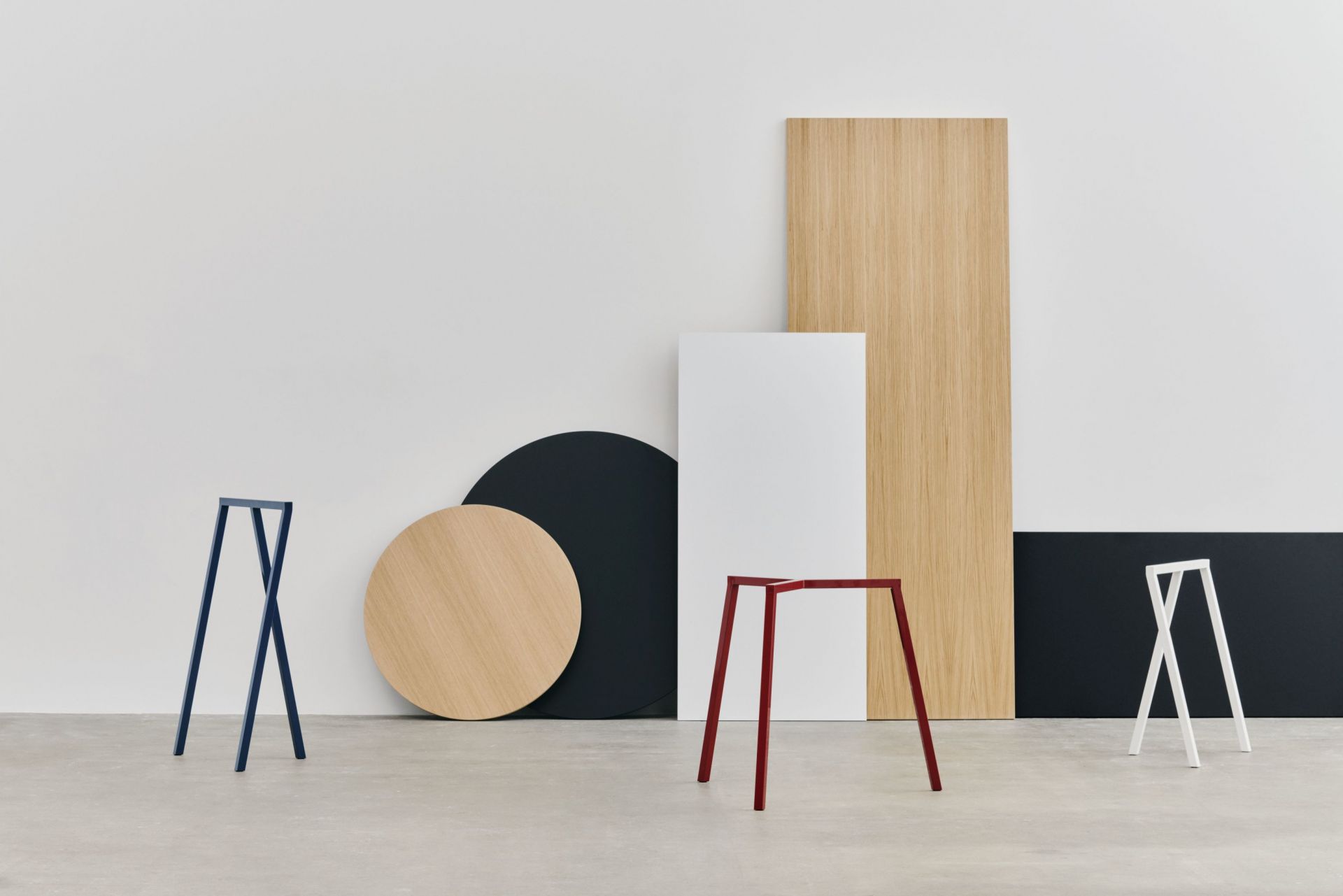 Drei farbige Loop Stand Frame Böcke von Hay vor geometrischen Formen in minimalistischem Design.