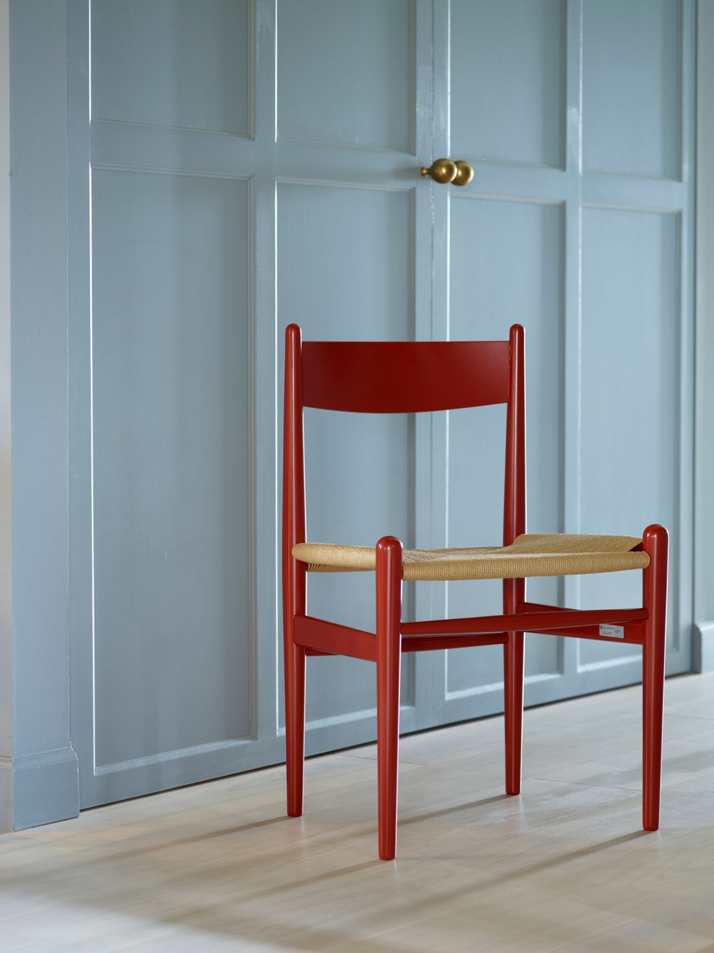 Roter CH36 Stuhl von Carl Hansen & Søn mit natürlichem Geflecht vor blauer Wand.