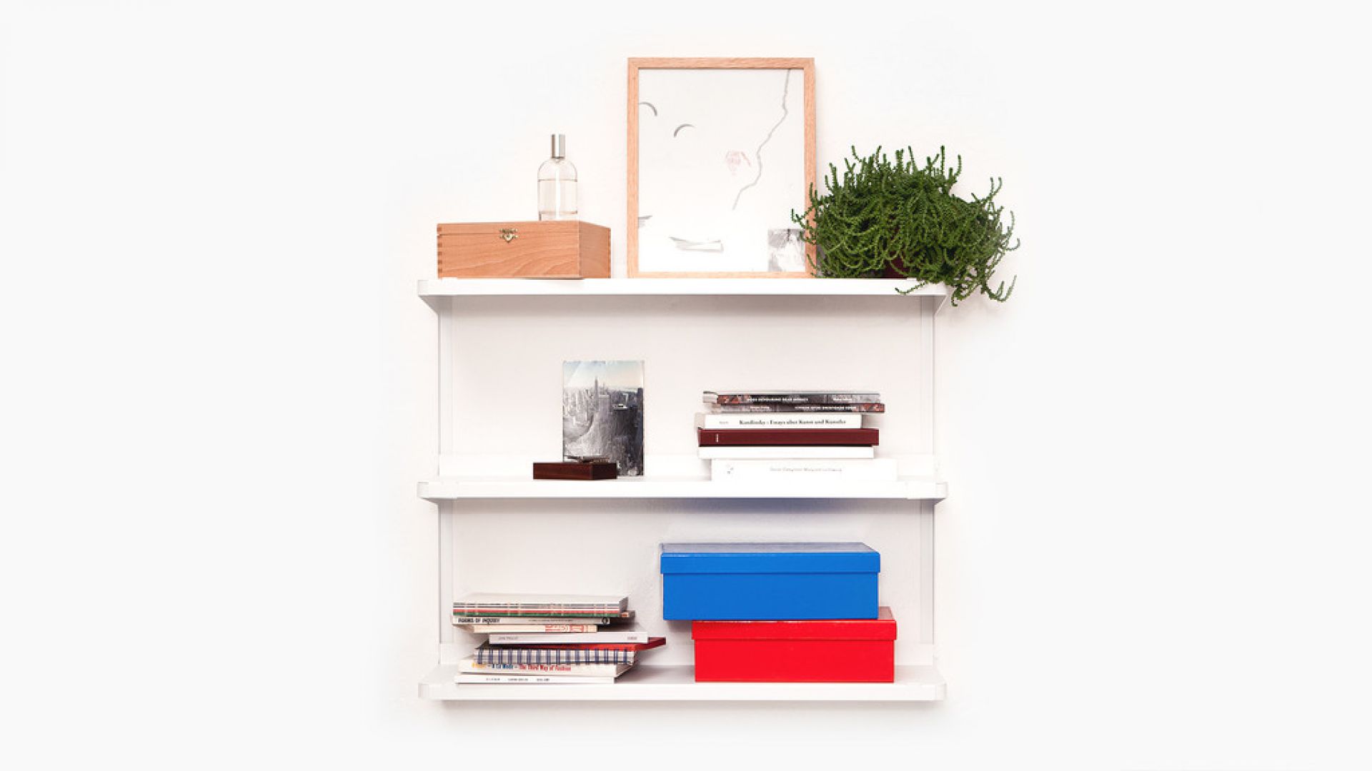 Weißes Click Wandregal von New Tendency mit Deko-Objekten, Büchern und bunten Boxen vor weißem Hintergrund.