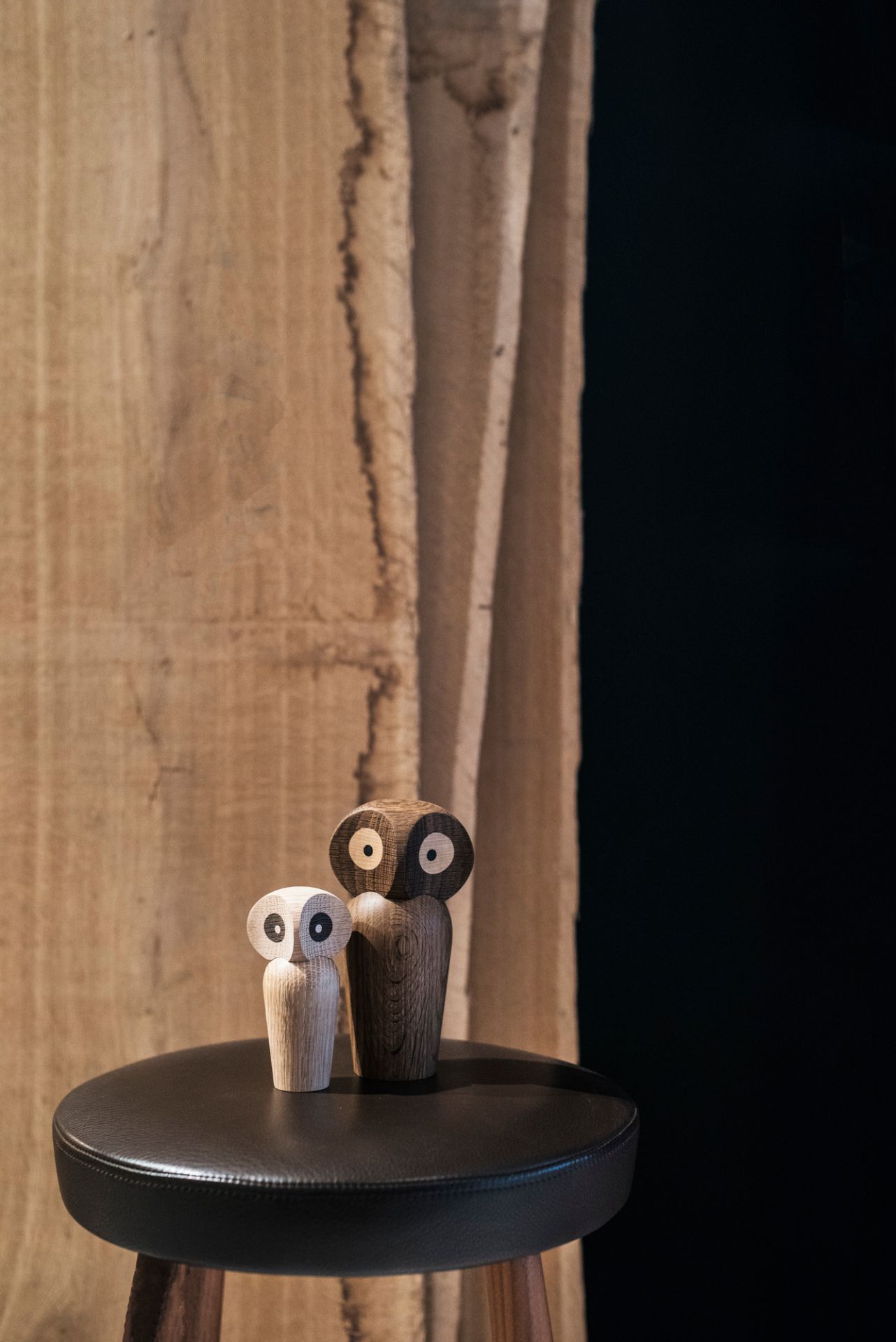Zwei Architectmade Holzfiguren Eulen, hell und dunkel, als Deko-Objekt auf einem Hocker.