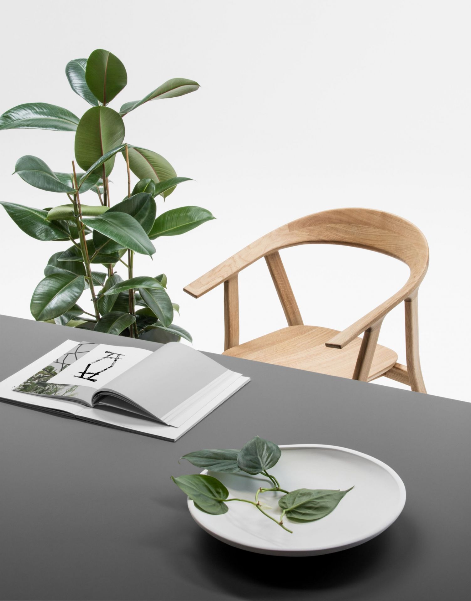 Rhomb Tisch von Prostoria mit Holzstuhl, Pflanze und Dekoration auf grauer Tischplatte.