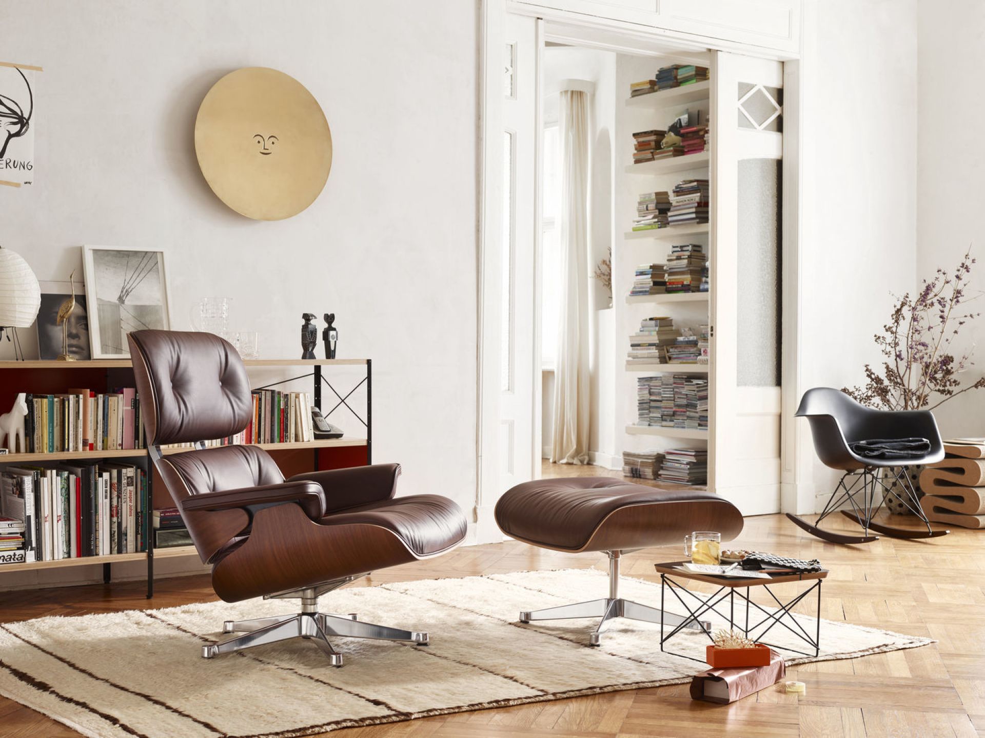 Wohnzimmer mit braunem Eames Sessel mit Sitzpolster und schwarzem Eames Schaukelstuhl im Hintergrund.