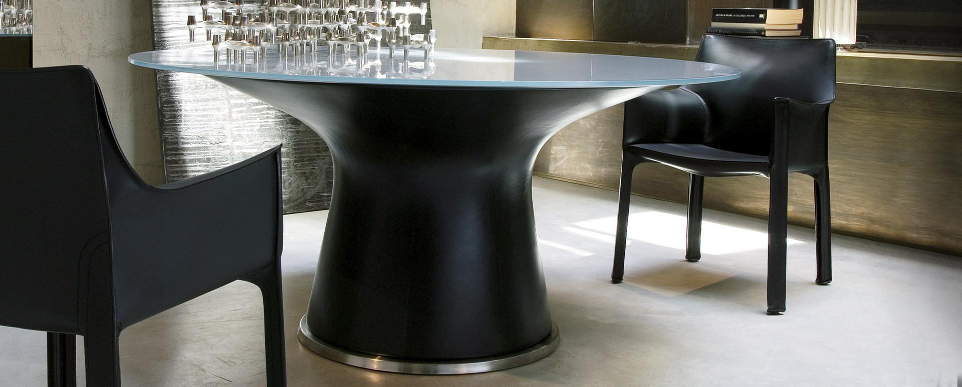 Schwarzer Cassina Cab Armchair Stuhl mit Armlehnen neben einem Esstisch mit Glasplatte.