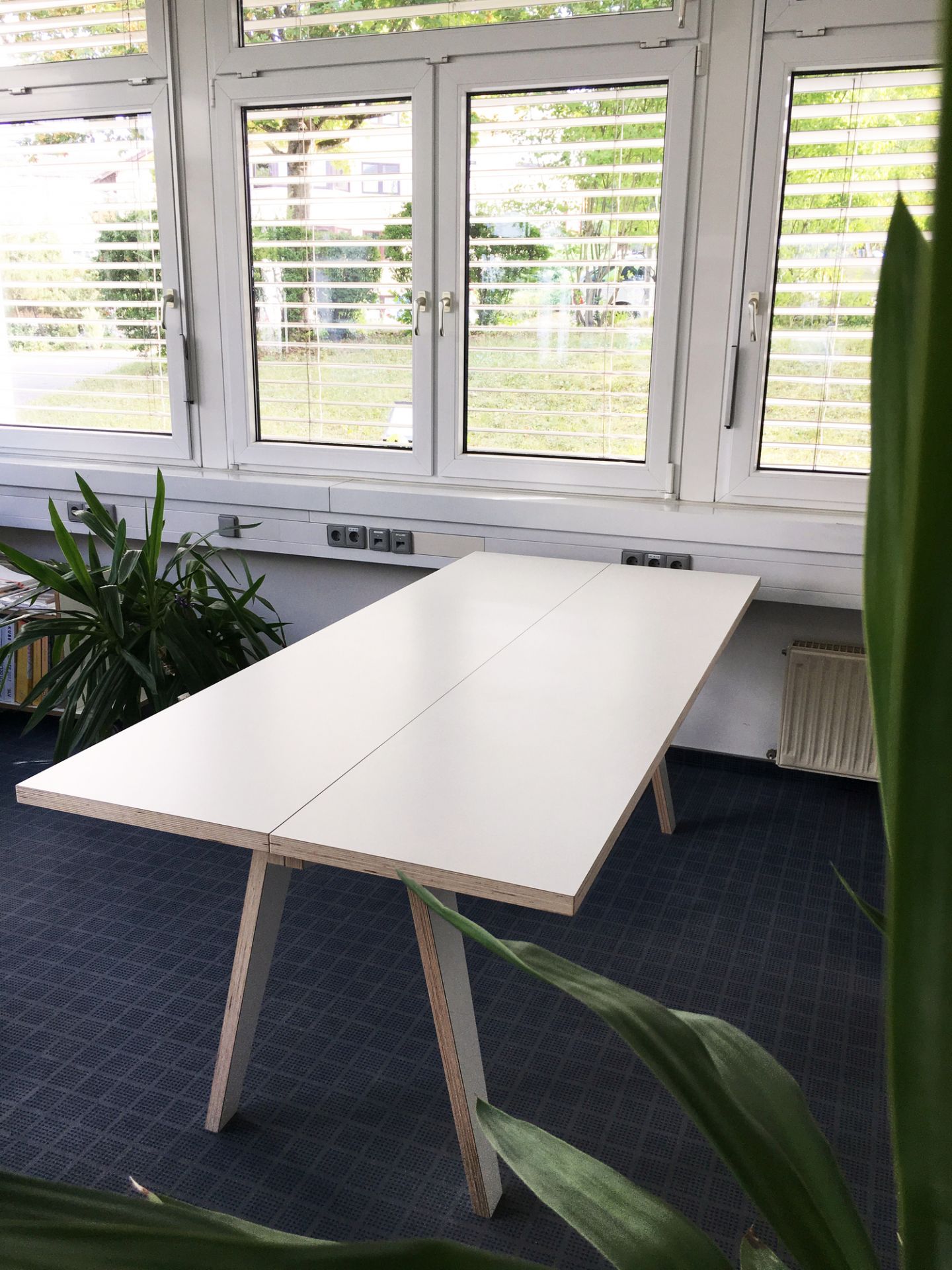 Weißer Tojo Tisch mit Holzbeinen vor einem Fenster, ideal als Schreibtisch oder Esstisch.