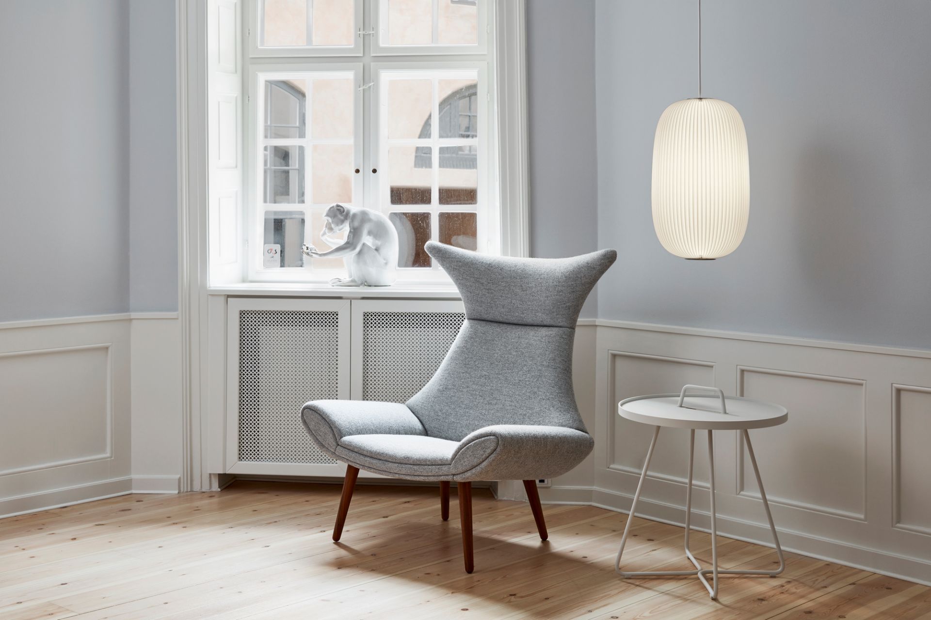 Helle Lamella Pendelleuchte von Le Klint in modernem Wohnzimmer mit Sessel und Beistelltisch.