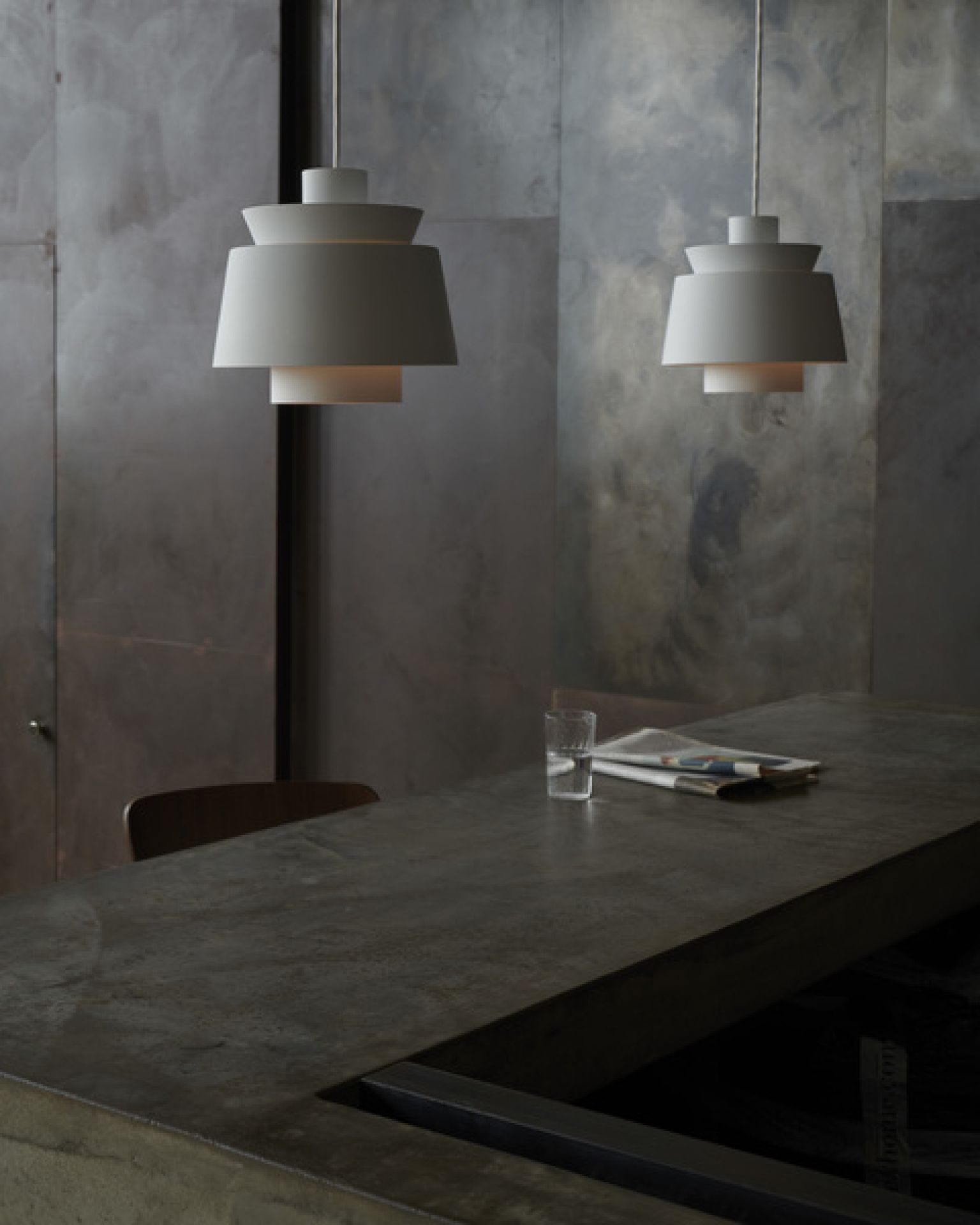 Zwei weiße Utzon Pendelleuchten von AndTradition hängen über einer modernen Küchentheke mit Zeitung und Wasserglas.