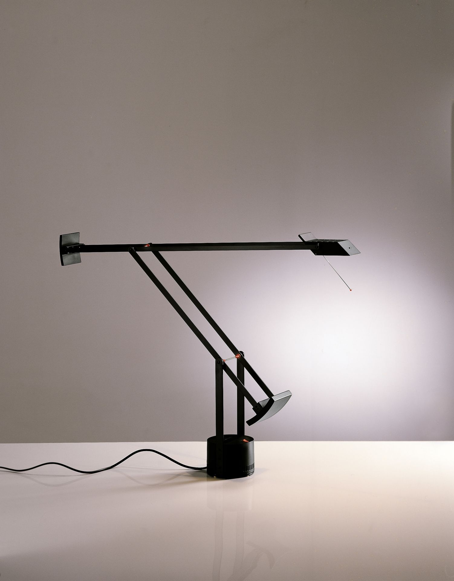 Schwarze Tizio Micro Tischleuchte von Artemide mit verstellbarem Arm und hellem Lichtschein auf einem Tisch.