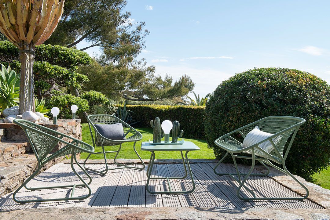 Grüne Sixties Outdoor Sessel und Tisch von Fermob auf einer Terrasse mit Garten im Hintergrund.