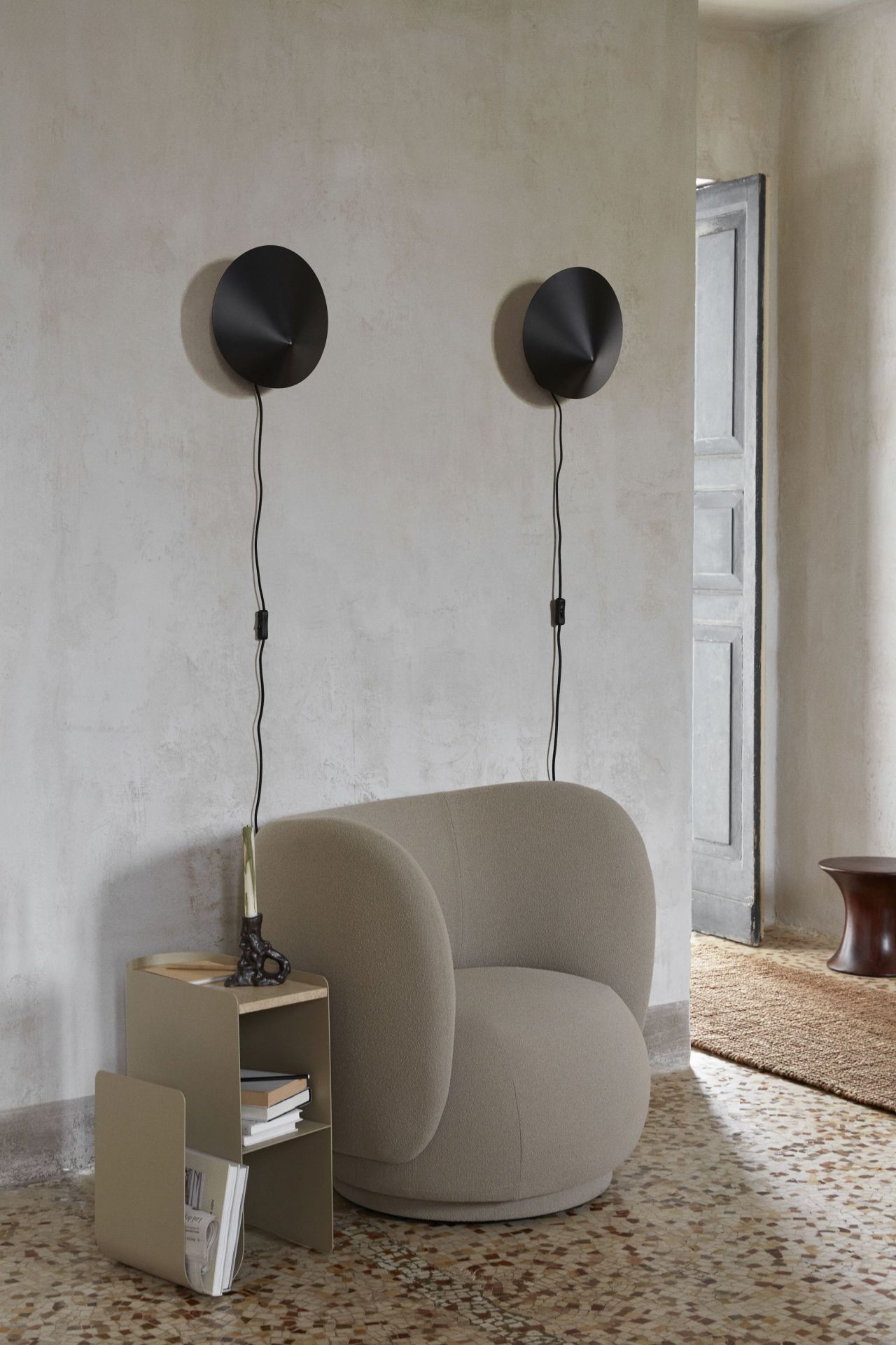 Zwei schwarze Arum Wandleuchten von Ferm Living über einem Sessel und Beistelltisch.