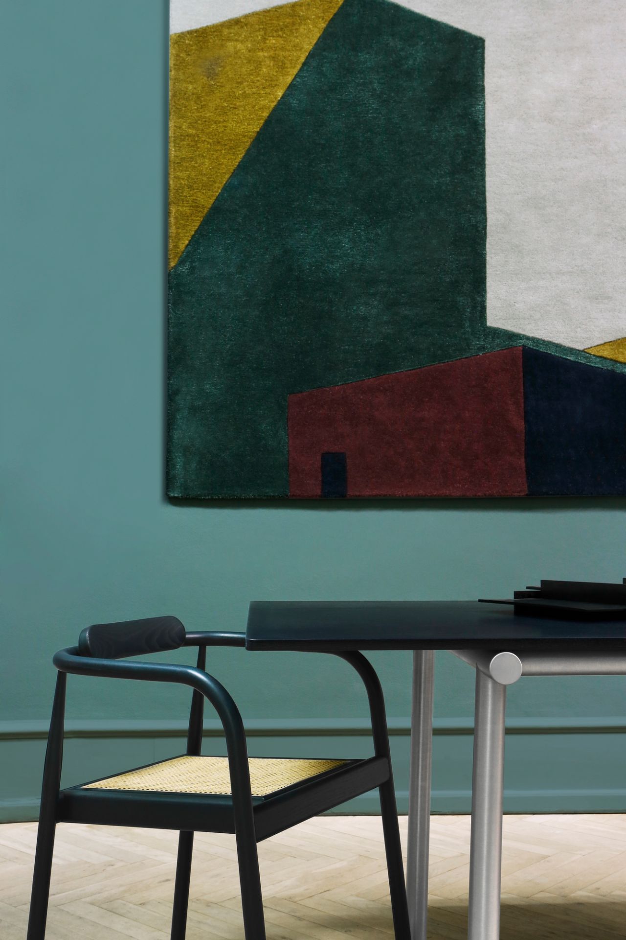 Arqui Teppich mit geometrischem Muster in Grün, Gelb und Rot an grüner Wand.