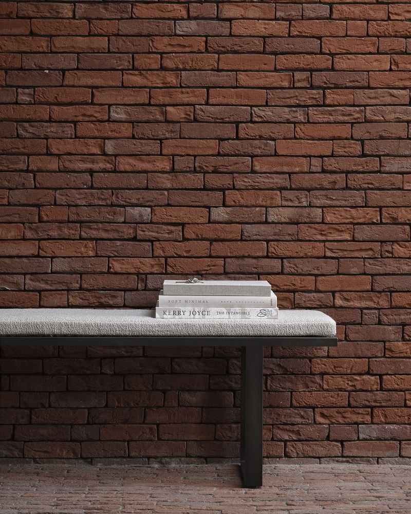 Stability Bank Natural Stoff Ethnicraft: Stoffbank mit Bücherstapel vor einer Backsteinwand.