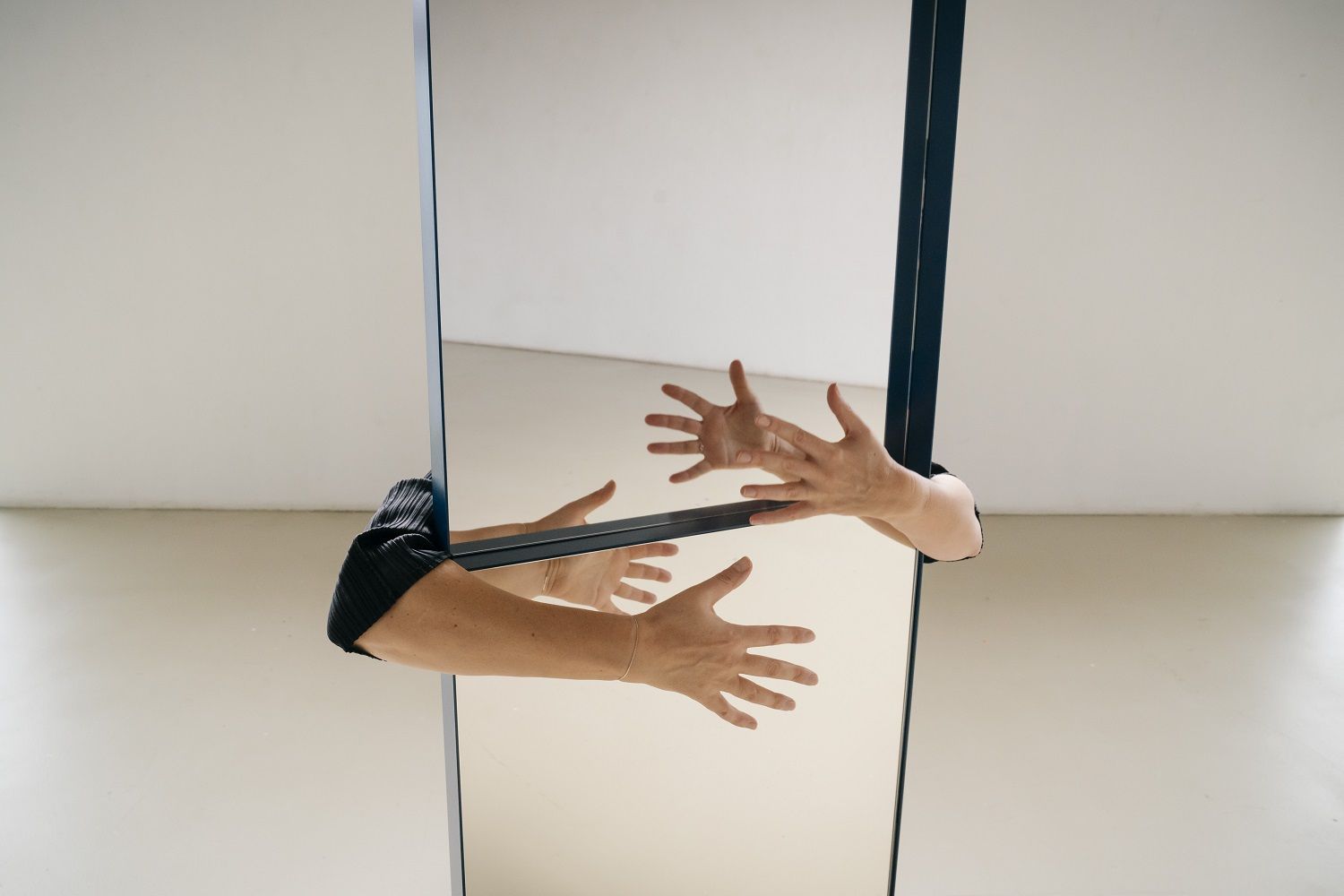 OneTwo Spiegel von Richard Lampert in Dunkelbronze mit Händen, die den Spiegel berühren.