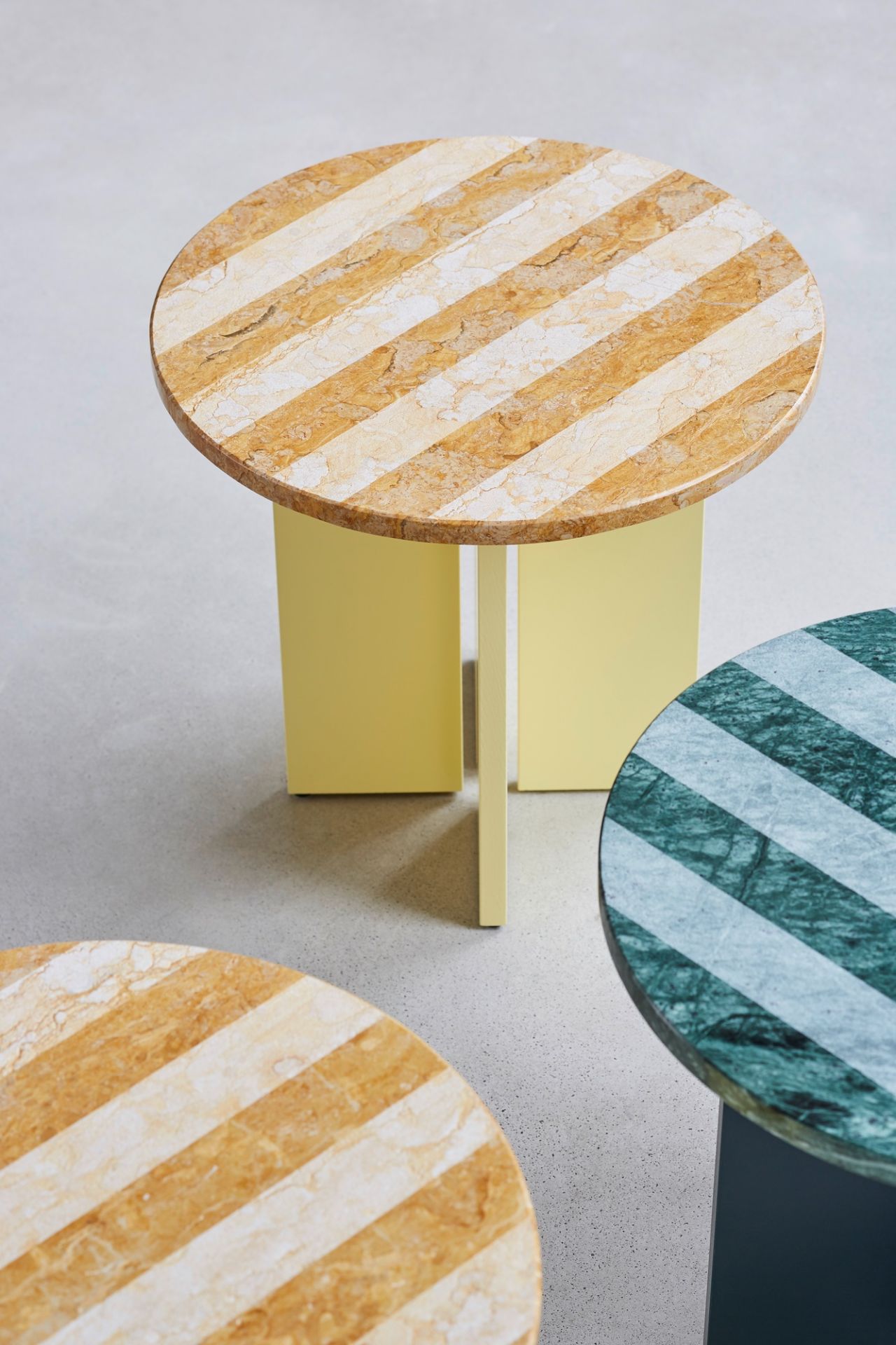 Sediment Beistelltisch mit runder Marmorplatte und gelbem Gestell, weitere Tische mit Marmor sichtbar.