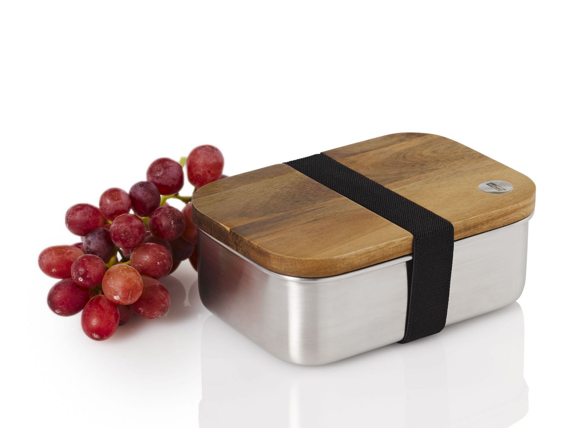AdHoc Lunchbox Cotto aus Edelstahl mit Holzdeckel und Gummiband, daneben rote Trauben.