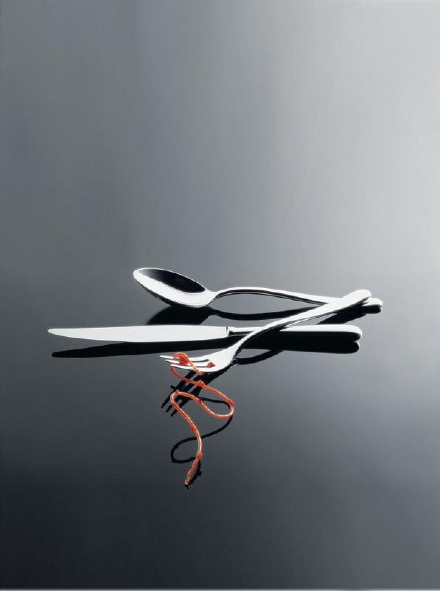 Alessi Caccia Besteck: Messer, Gabel und Löffel aus Edelstahl auf glänzendem Untergrund. Hochwertiges Besteckset für stilvolles Essen.