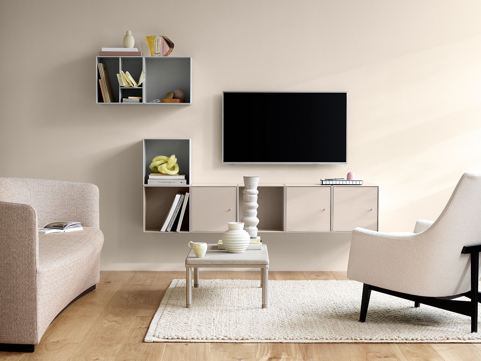 Modernes Wohnzimmer mit TV-Wand, Regalen, Teppich, Couch und Sessel in Beige- und Weißtönen.