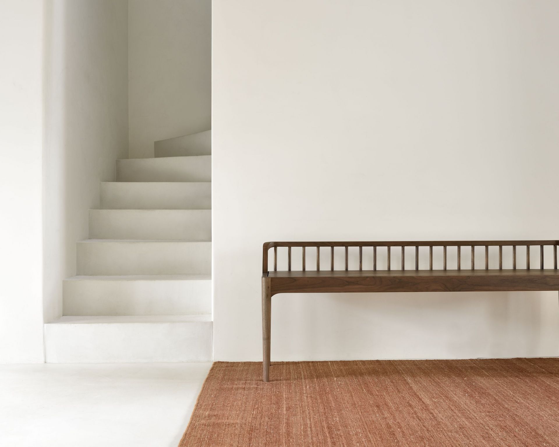 Terracotta Nomad Kilim Teppich von Ethnicraft unter einer Holzbank in minimalistischem Raum mit Treppe.