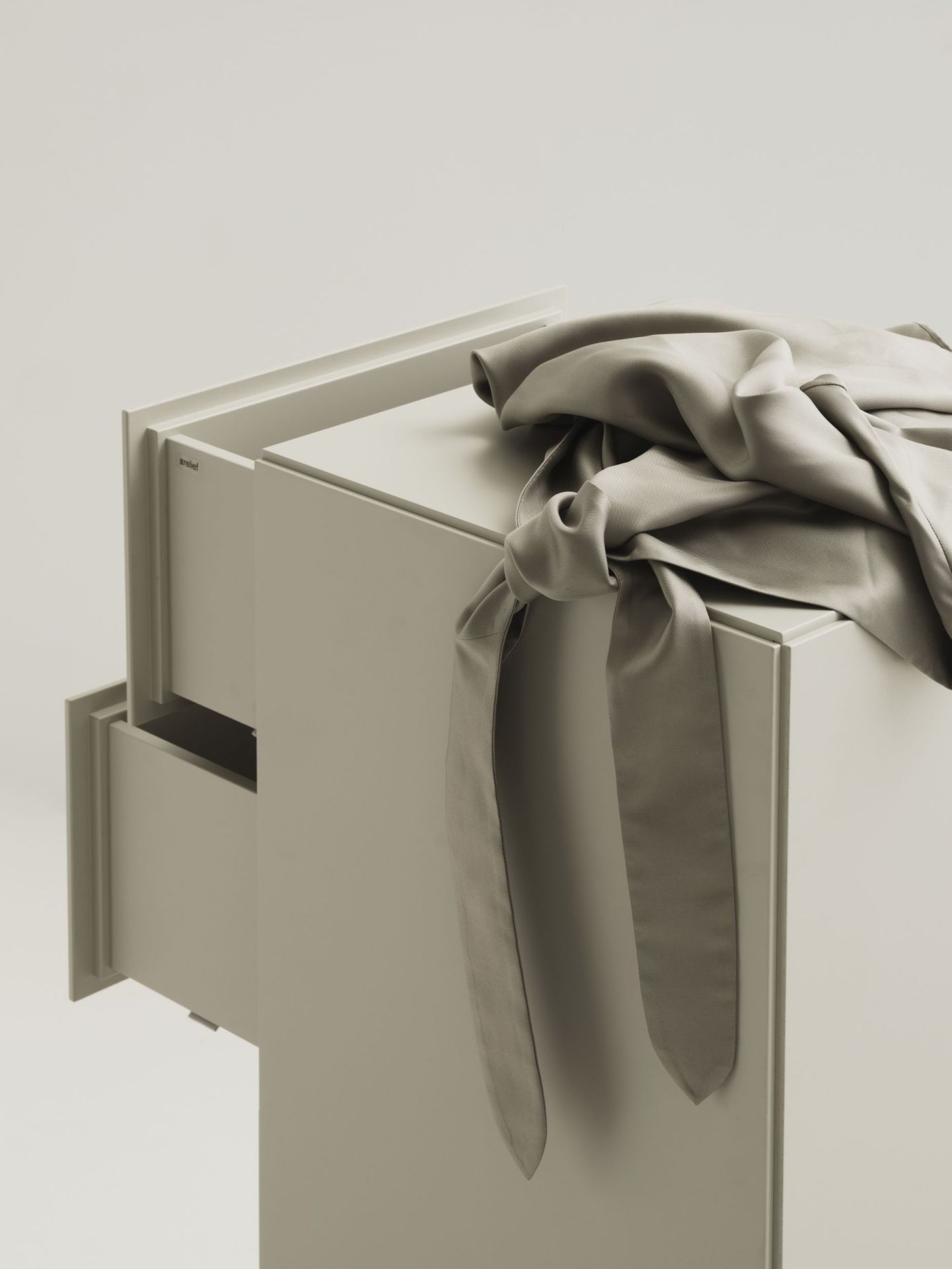 Beige Relief Kommode von String Furniture mit Schublade und drapiertem Stoff.