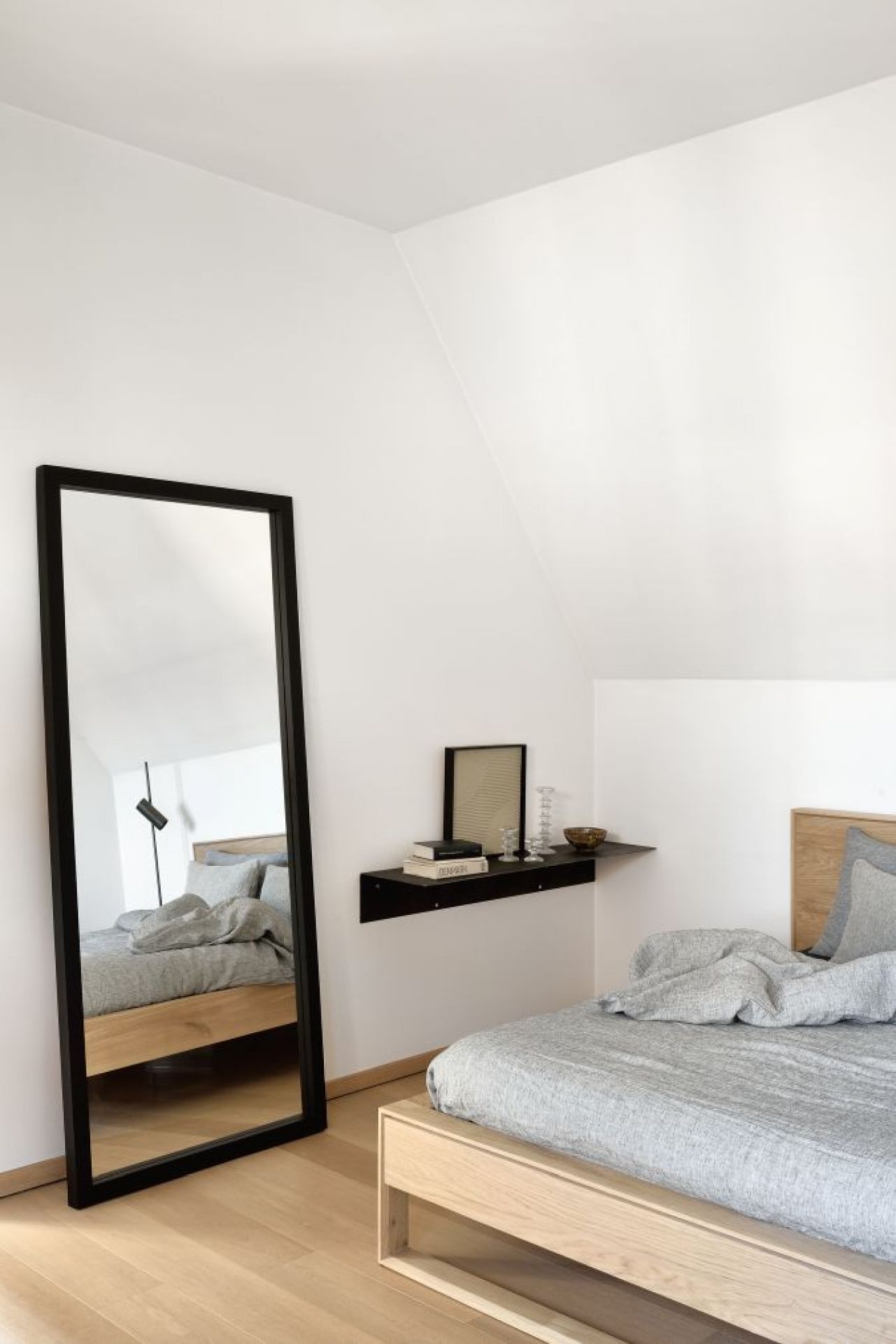 Schlafzimmer mit Ethnicraft Spiegel, Eiche-Rahmen in Schwarz, der das Bett reflektiert.