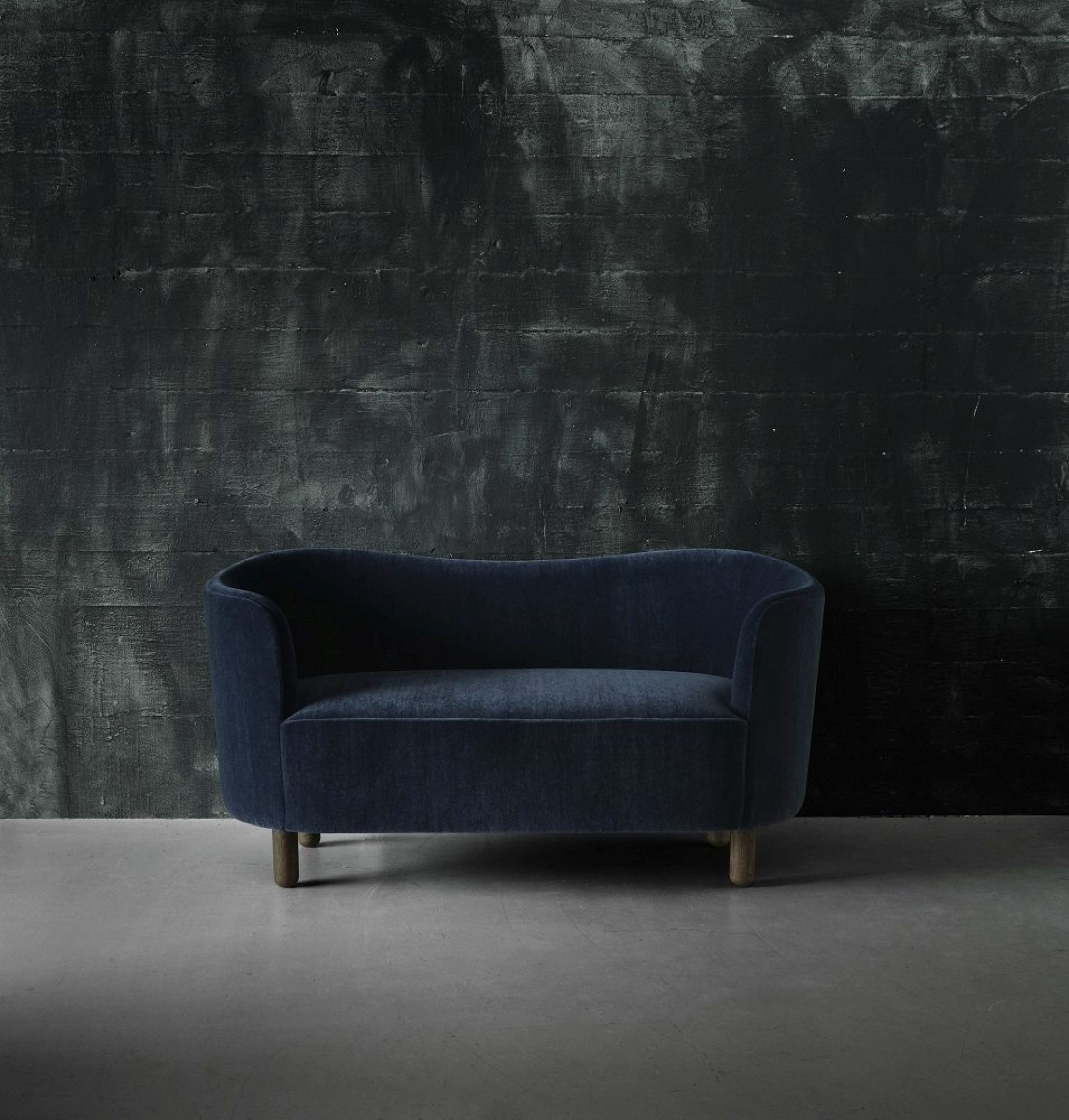 Blaues Mingle Sofa von Audo, ein Zweisitzer-Sofa mit dunklem Hintergrund und Holzfüßen.