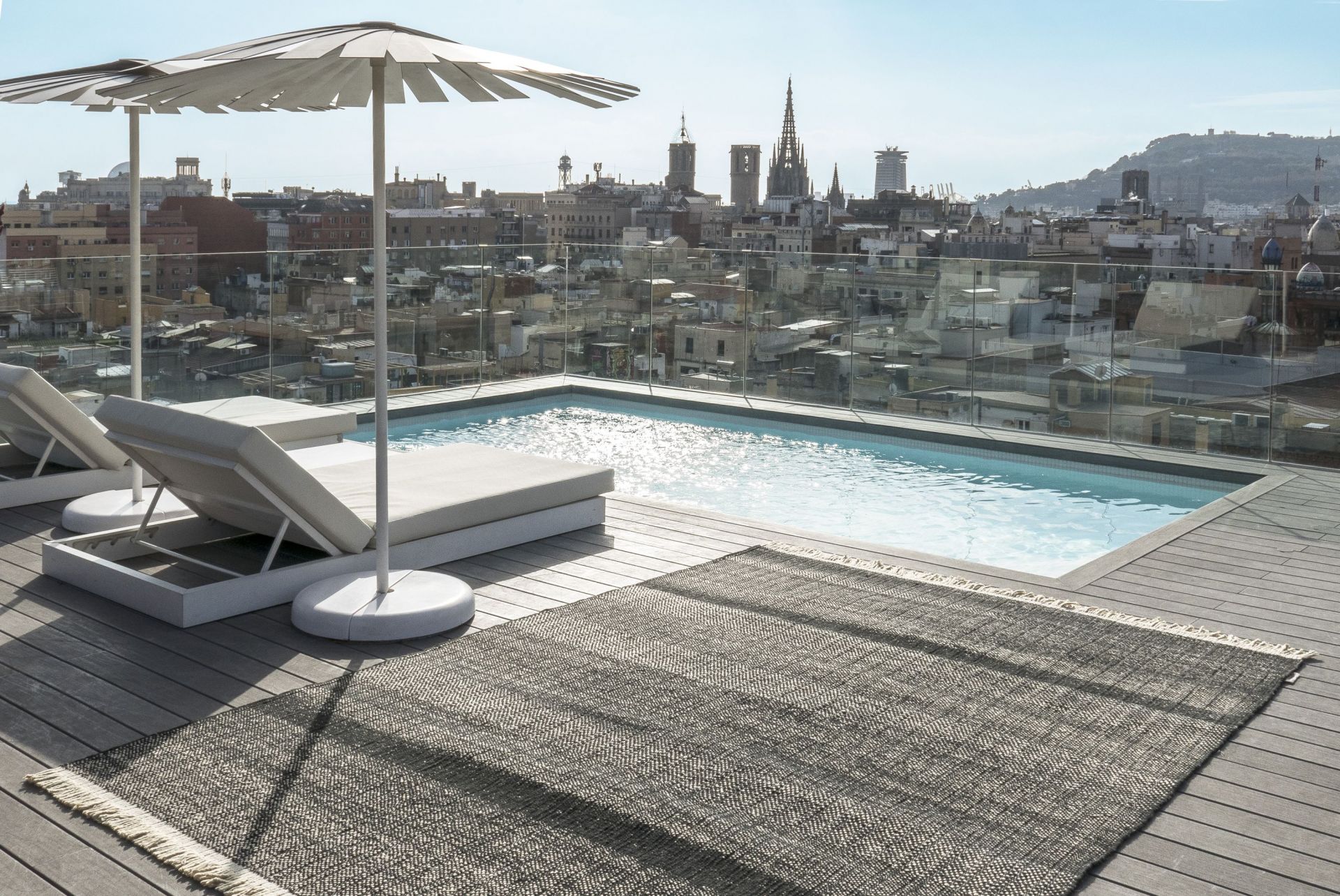 Nanimarquina Tres Outdoor Texture Teppich Schwarz 250x350 cm auf einer Dachterrasse mit Pool und Stadtblick.
