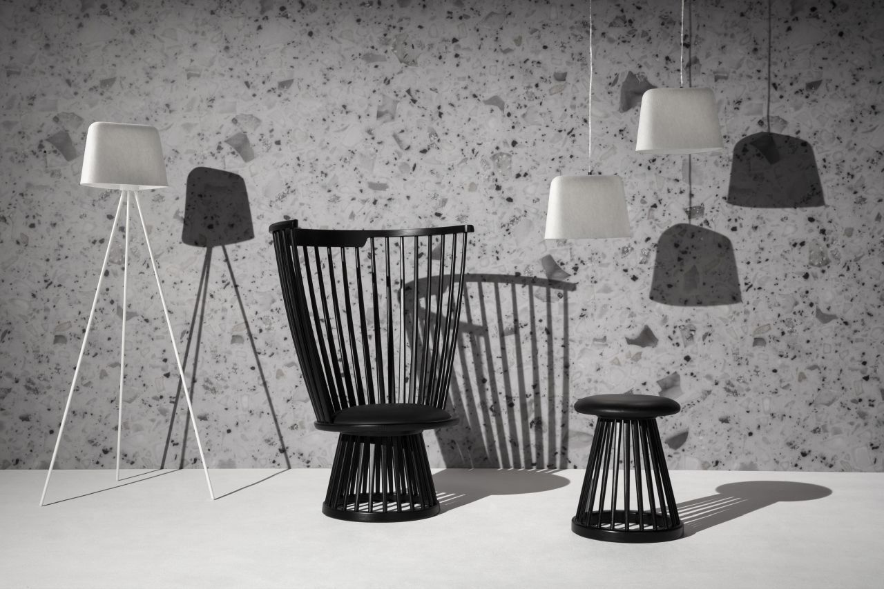 Schwarzer Tom Dixon Hocker mit Lamellenstruktur, passender Stuhl und Stehlampe vor gemusterter Wand.