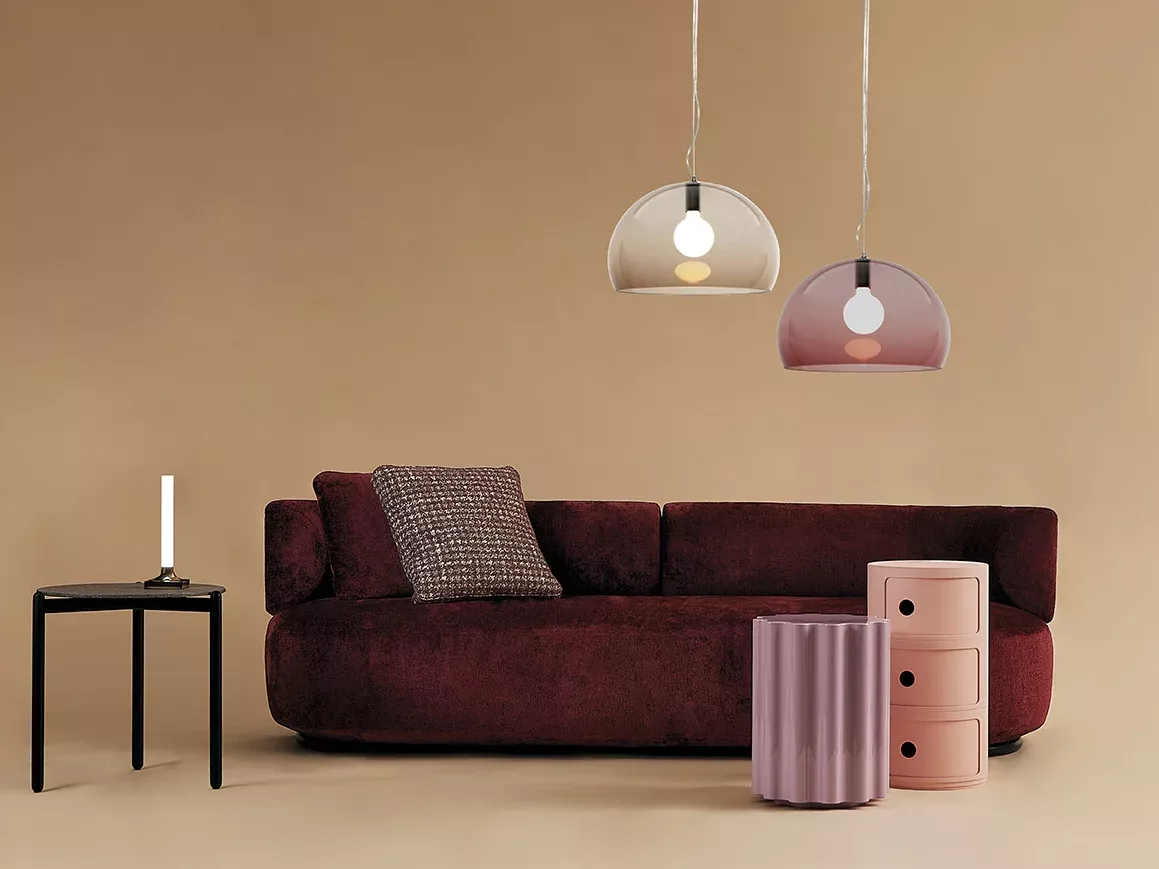 Zwei Kartell Fl/Y Pendelleuchten in Braun und Rosa über einem roten Sofa.