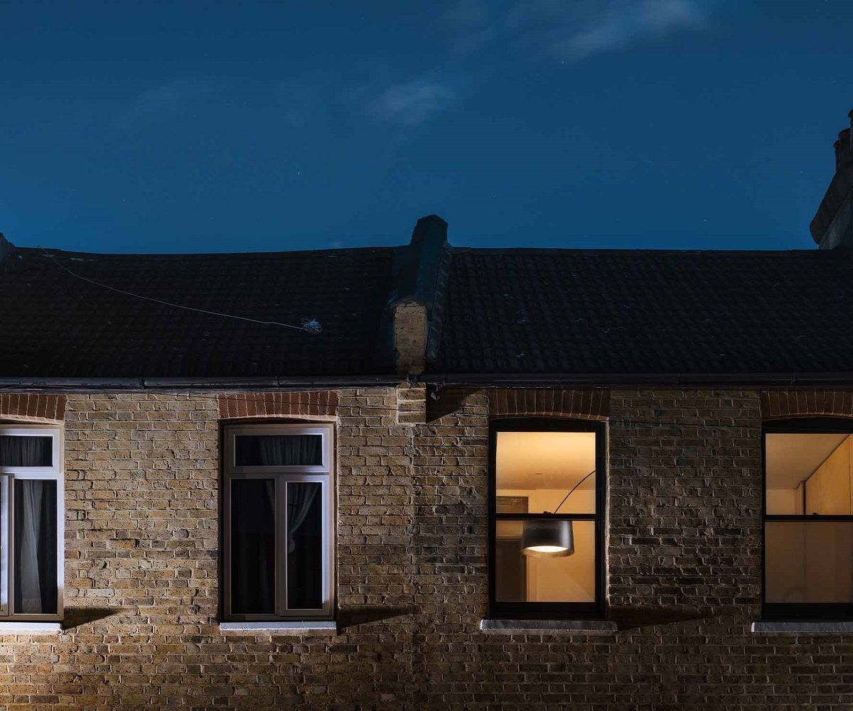 Foscarini Twiggy Soffitto Deckenleuchte, modernes Design, schwarzer Lampenschirm, Innenansicht durch Fenster eines Backsteinhauses bei Nacht.