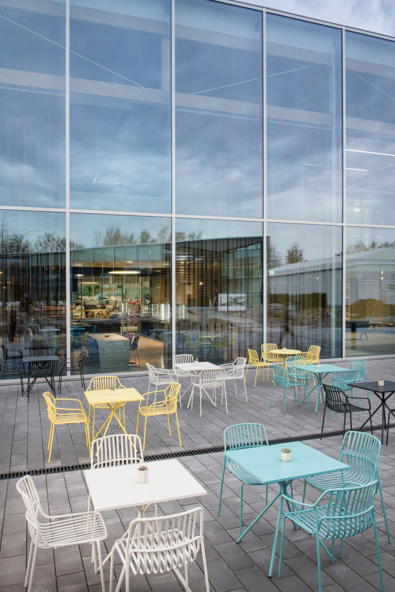 Quadratische Crona Steel Bistrotische von Brunner in verschiedenen Farben für den Außenbereich, vor Glasfassade.