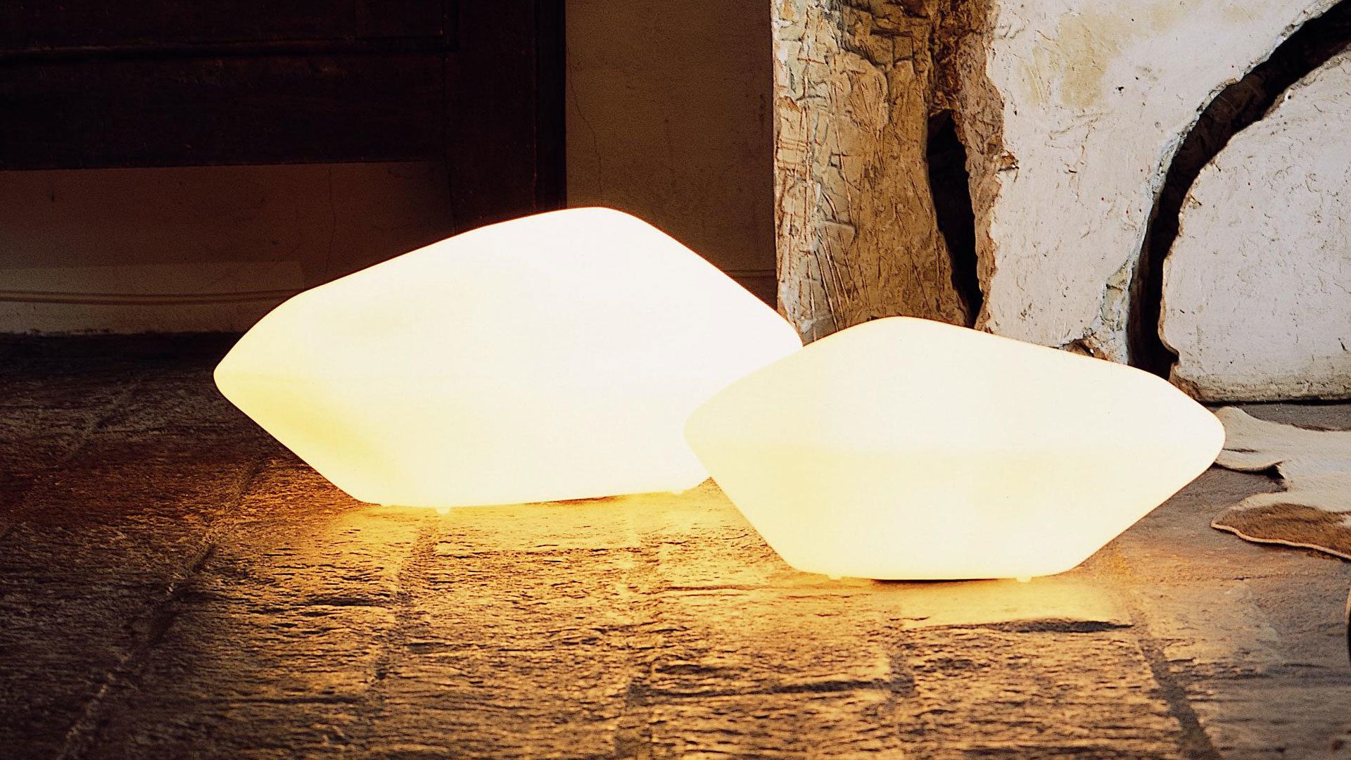 Zwei leuchtende Stone of Glass Bodenleuchten von Oluce im Außenbereich, warmes Licht.