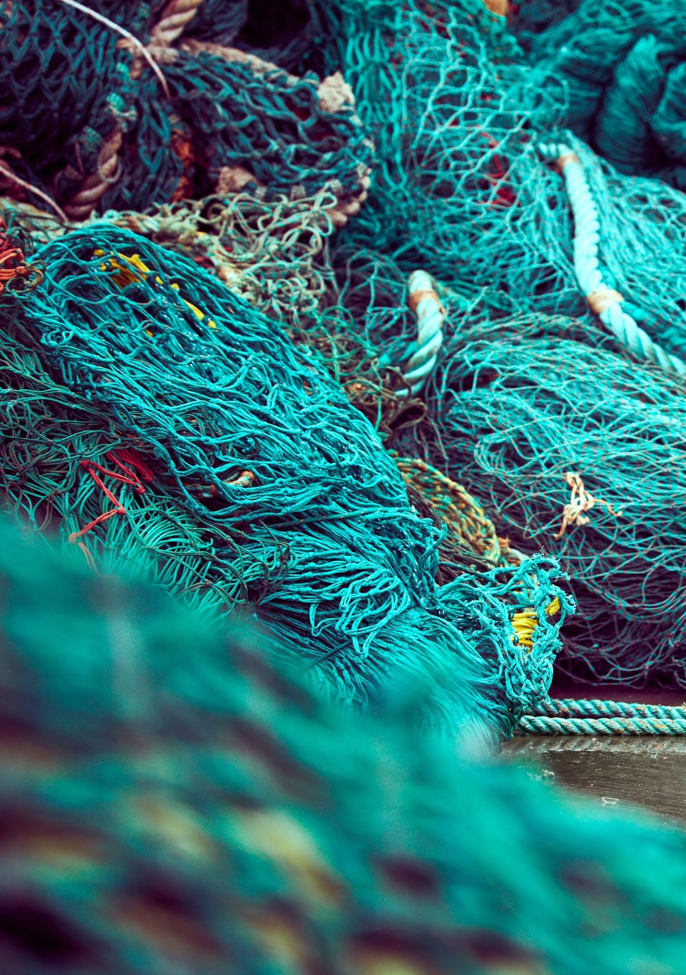 Nahaufnahme von türkisfarbenen Fischernetzen und Seilen, die übereinander gestapelt sind.