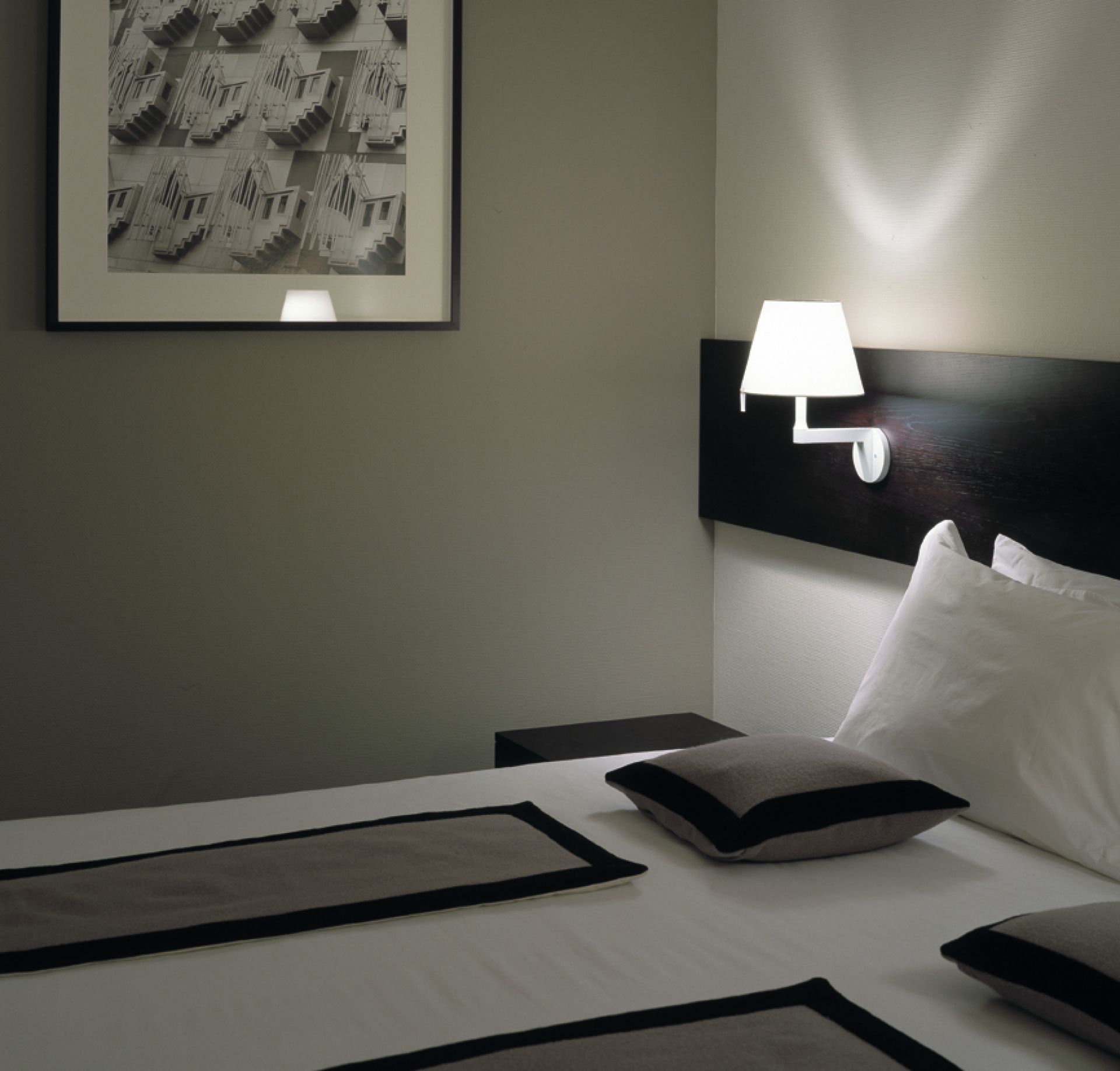 Nahaufnahme einer weißen Melampo Wandleuchte von Artemide über einem Bett.