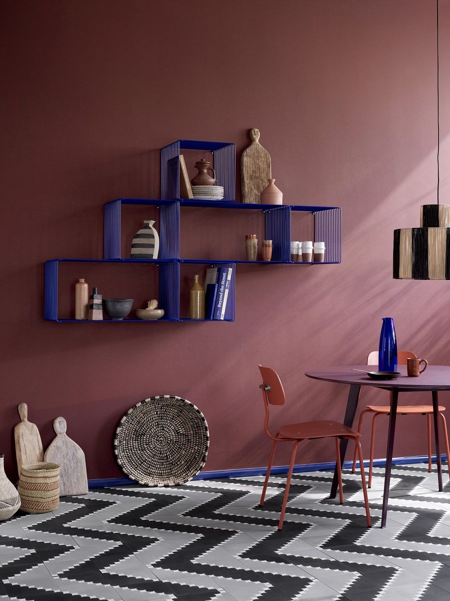 Blaues Montana Wire Cube Drahtregal an einer roten Wand, dekoriert mit Vasen und Deko-Objekten.