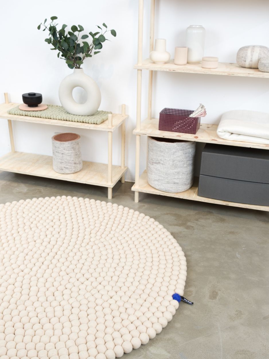 Beiger, runder myfelt Filzteppich "Big One" (Ø 160 cm) im Interieur mit Regalen. Handgefertigter Wollteppich.