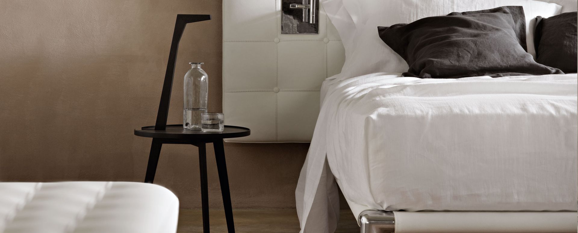 Cicognino Beistelltisch Esche amarant von Cassina neben einem Bett mit Wasserflasche und Glas.