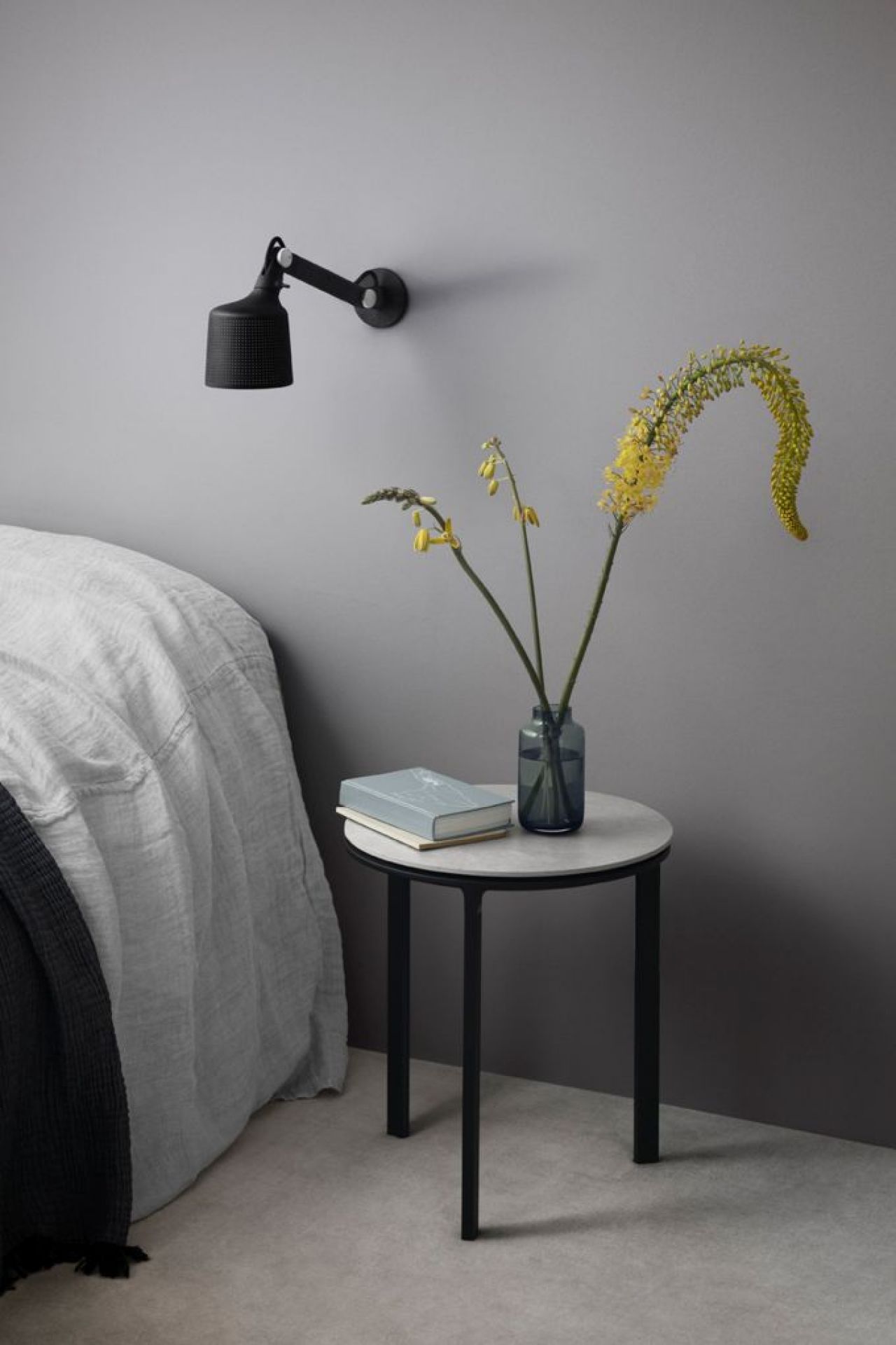 Nahaufnahme einer kleinen schwarzen Vipp Wandlampe über einem Nachttisch im Schlafzimmer.