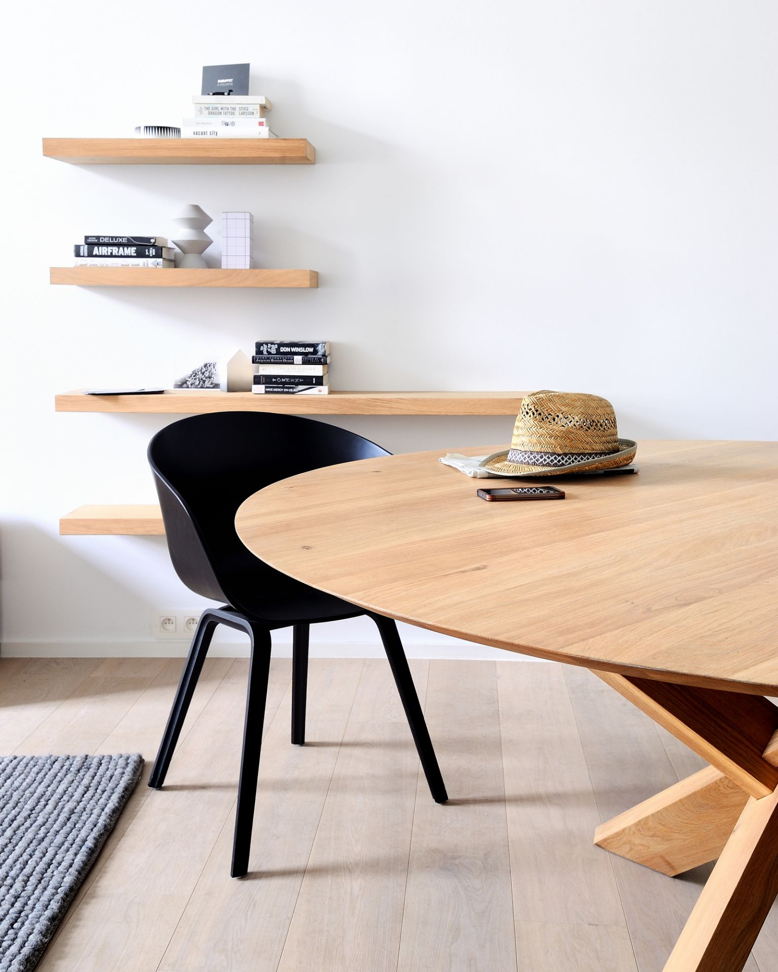 Helles Wohnzimmer mit Ethnicraft Wandregal aus Eiche, rundem Holztisch, Stuhl und Dekoration.