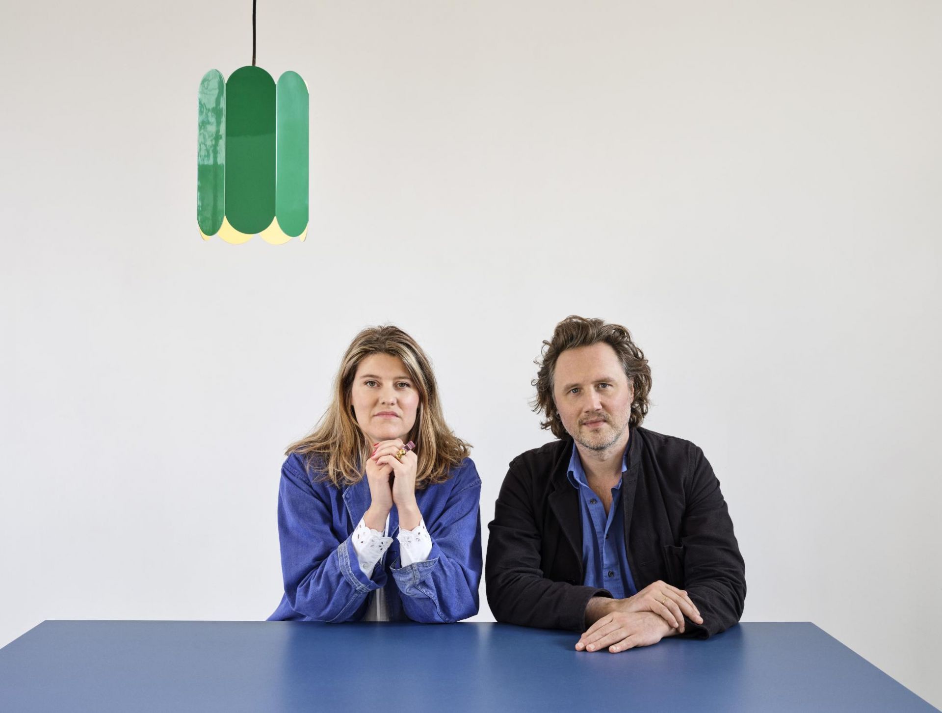 Zwei Personen sitzen am Two Colour Table Tisch von Hay in Blau, darüber eine grüne Lampe.