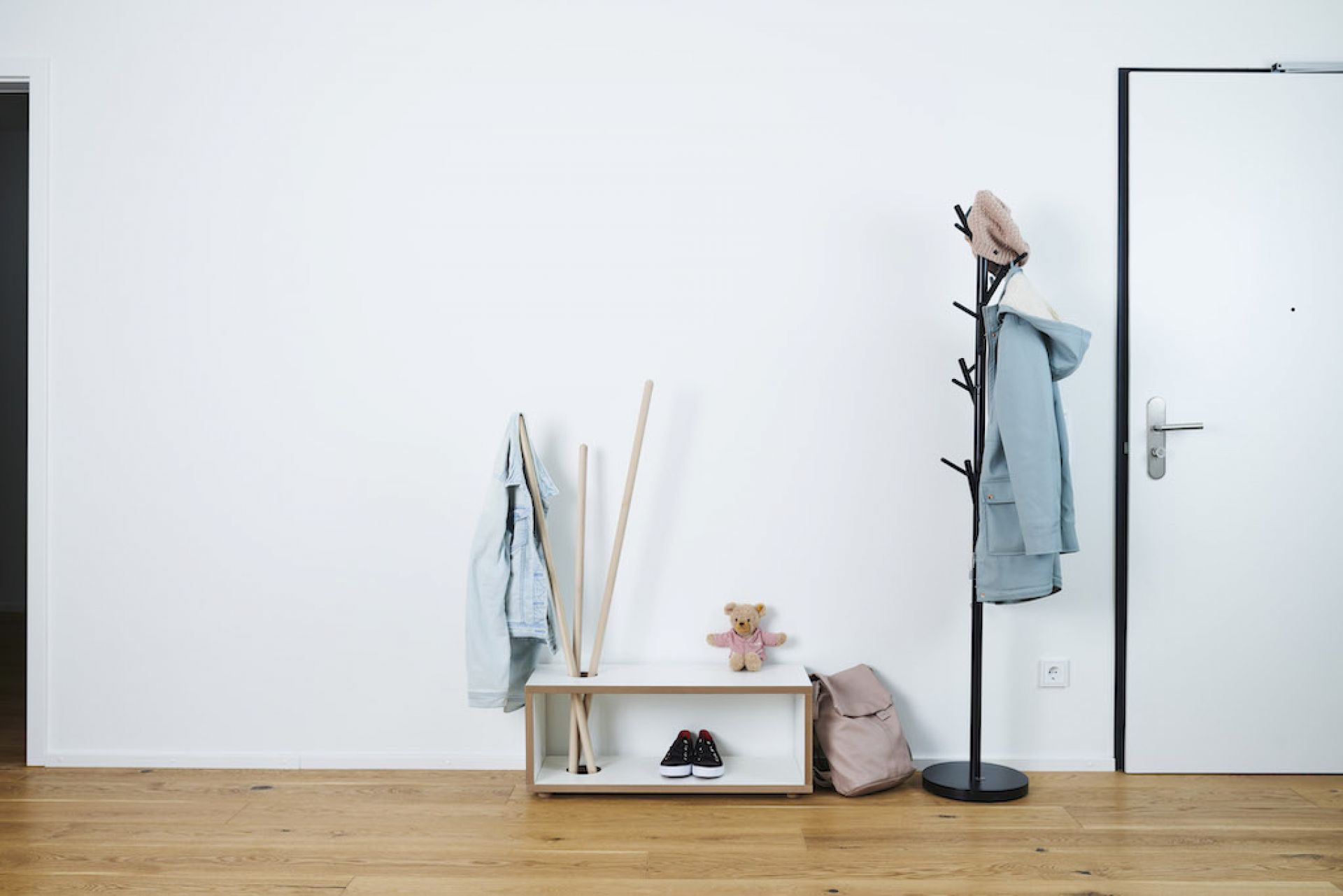 Tojo Kids Ordnung Kindergarderobe mit Jacken, Schuhen, Rucksack und Teddybär vor weißer Wand und Tür.