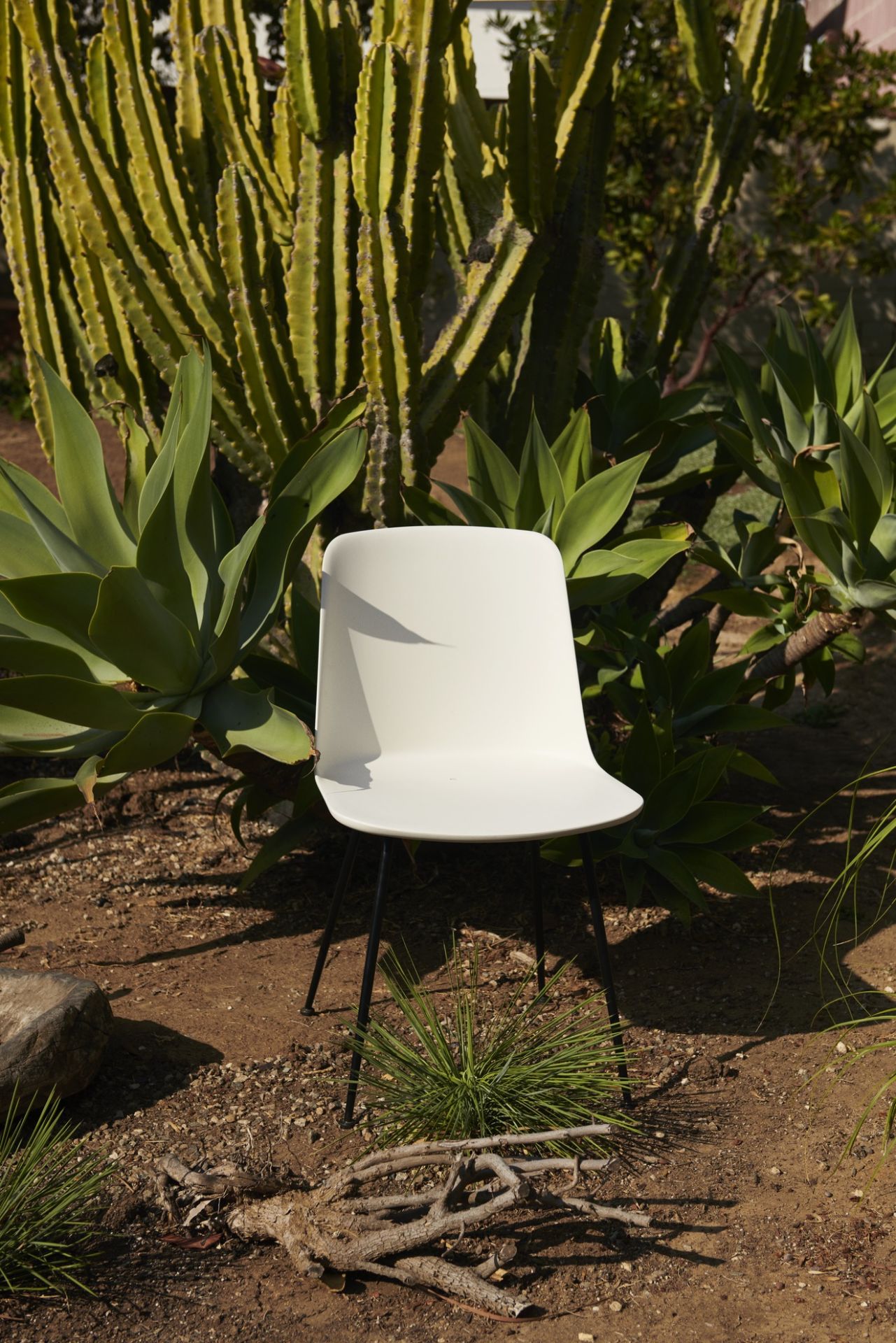 Weißer Rely HW70 Outdoor Stuhl von AndTradition im Garten, umgeben von Pflanzen und Kakteen.