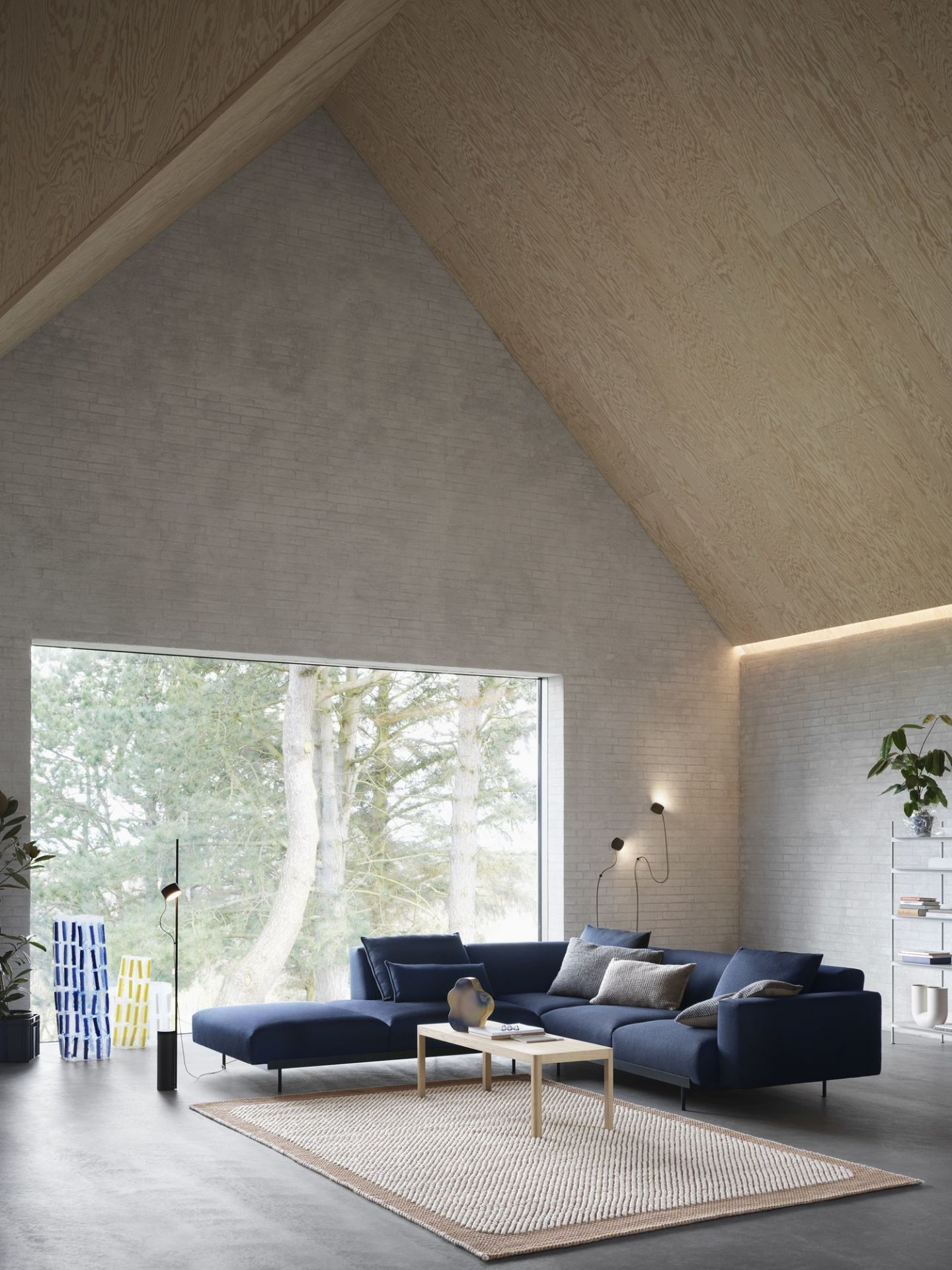 Wohnzimmer mit Muuto Post Wall Lamp Wandleuchten und blauem Ecksofa vor großem Fenster.