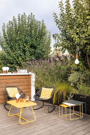 Zwei schwarze Sixties Schaukelstühle mit gelben Kissen und gelbem Tisch auf einer Holzterrasse.