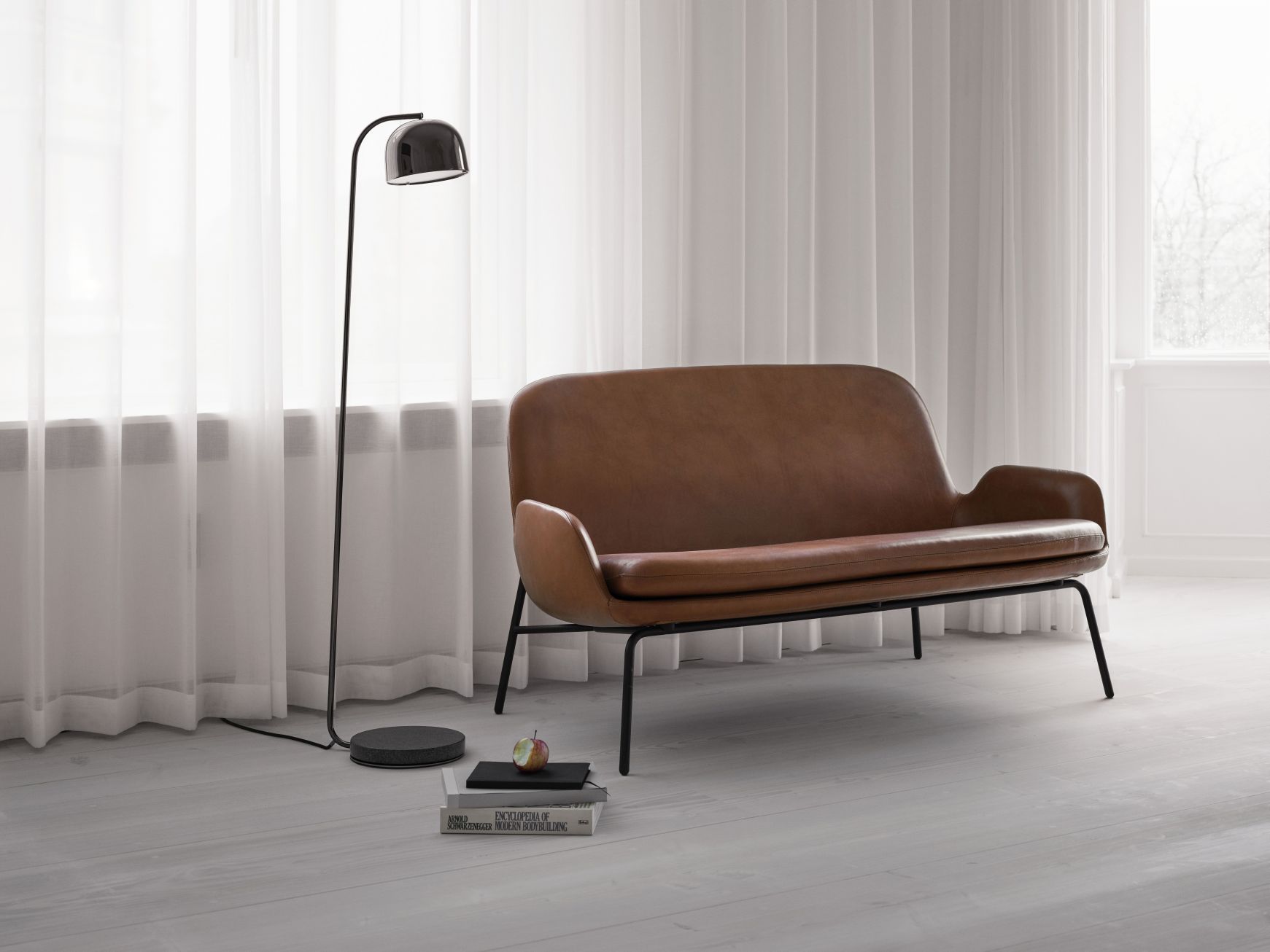 Braunes Era Sofa von Normann Copenhagen mit schwarzem Gestell und Stehlampe.