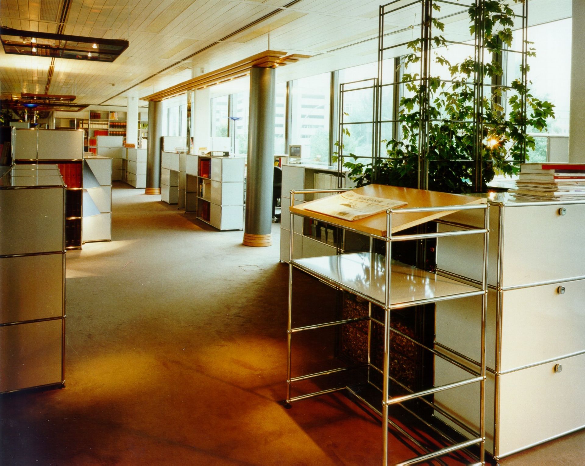 Helles Büro mit USM Haller Möbeln: Stehpult mit Holzplatte und Regalen, Aktenschränke im Hintergrund.