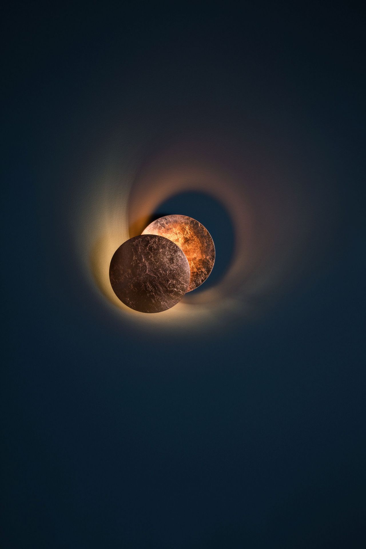 Lederam Wandleuchte von Catellani & Smith: Zwei runde, beleuchtete Scheiben an dunkler Wand.