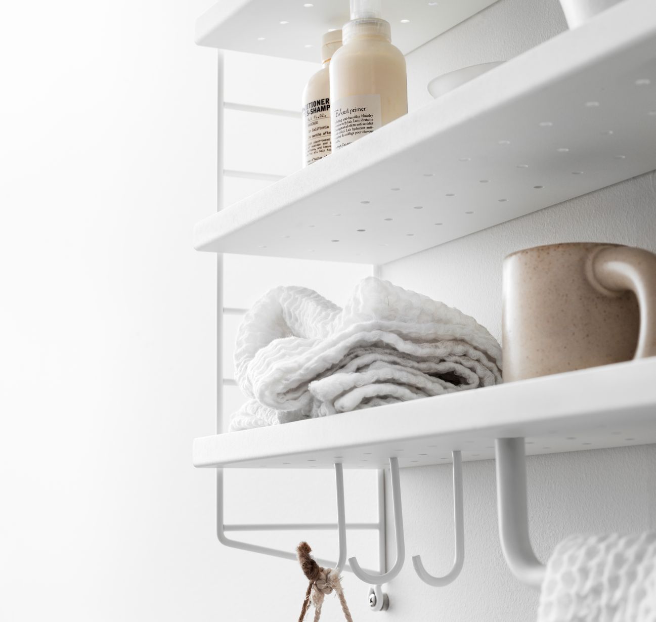 Detailaufnahme eines weißen Metallregals (String Furniture ähnlich) mit Handtuch, Tasse und Badutensilien.