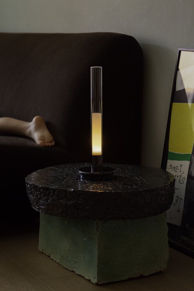 Sylvestrina Tischleuchte von Santa Cole auf einem Beistelltisch, warmes Licht, modernes Design.