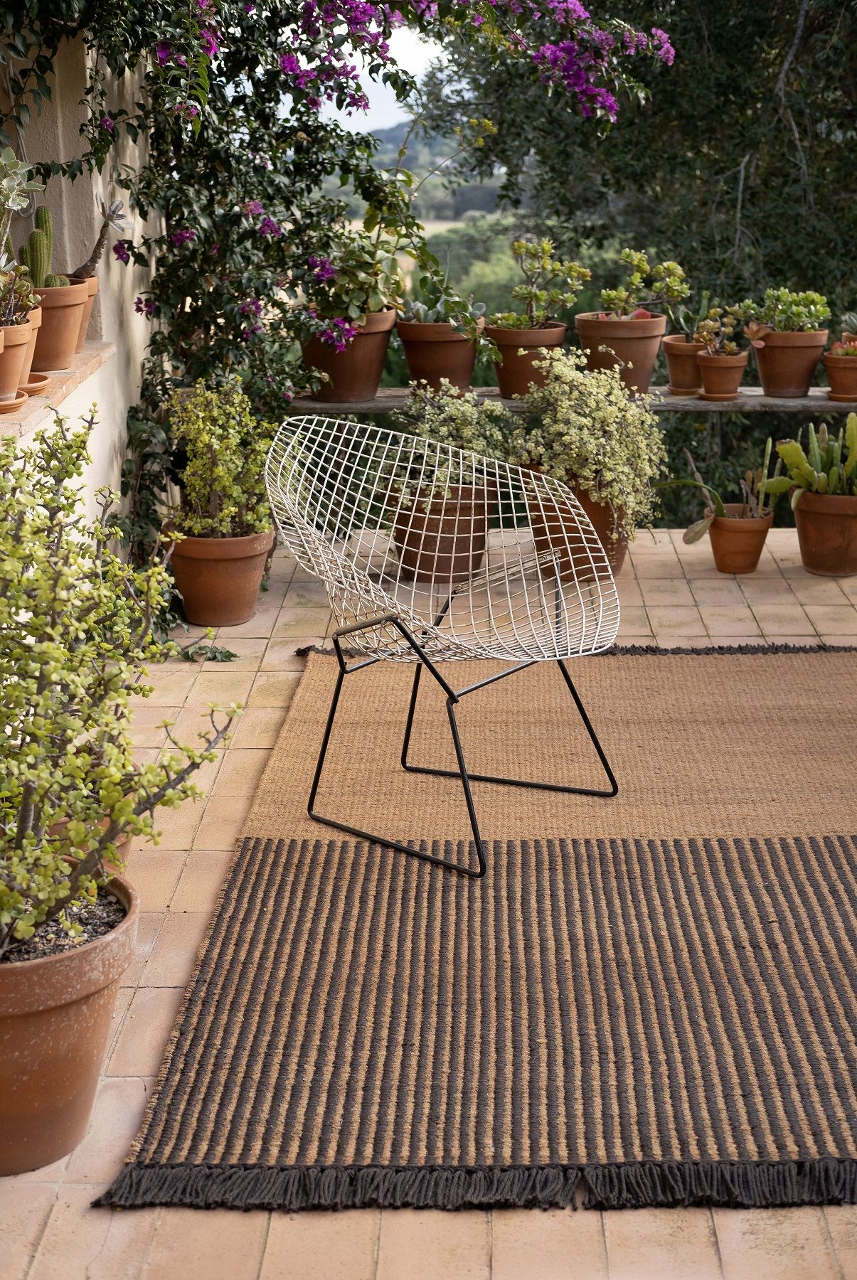 Nanimarquina Garden Outdoor Teppich in Schwarz mit Streifenmuster auf einer Terrasse mit Pflanzen.